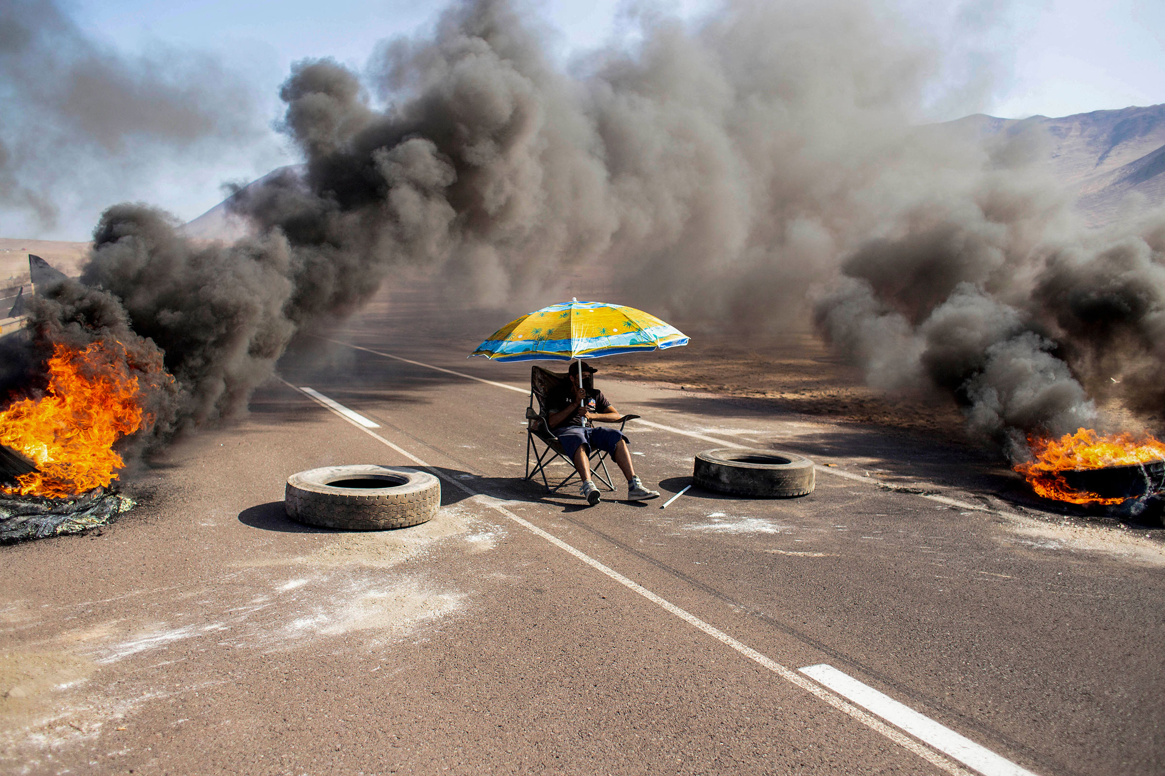 A demonstrator sits under an umbrella while blocking an access route to Iquique, Chile, during a regional strike called by different organizations against illegal immigration, on Jan. 31. (Diego Reyes—AFP/Getty Images)