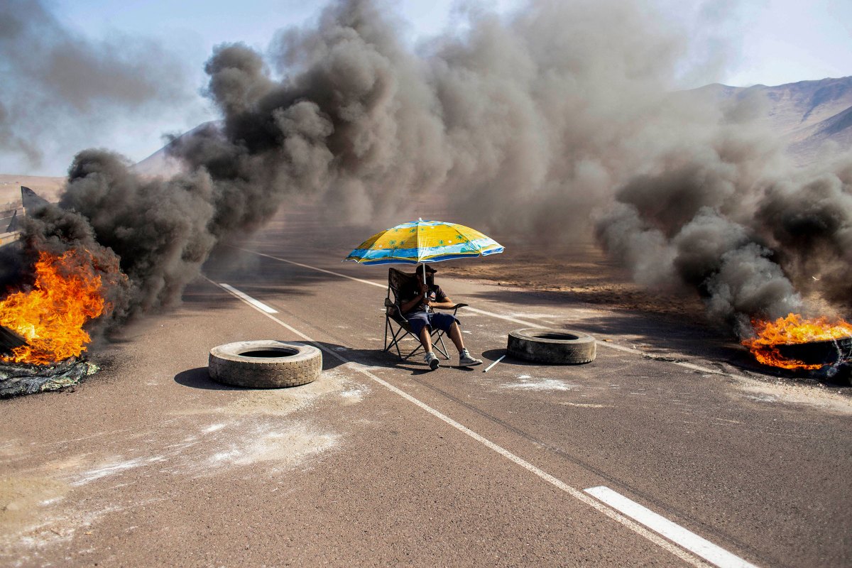 A demonstrator sits under an umbrella while blocking an access route to Iquique, Chile, during a regional strike called by different organizations against illegal immigration, on Jan. 31.