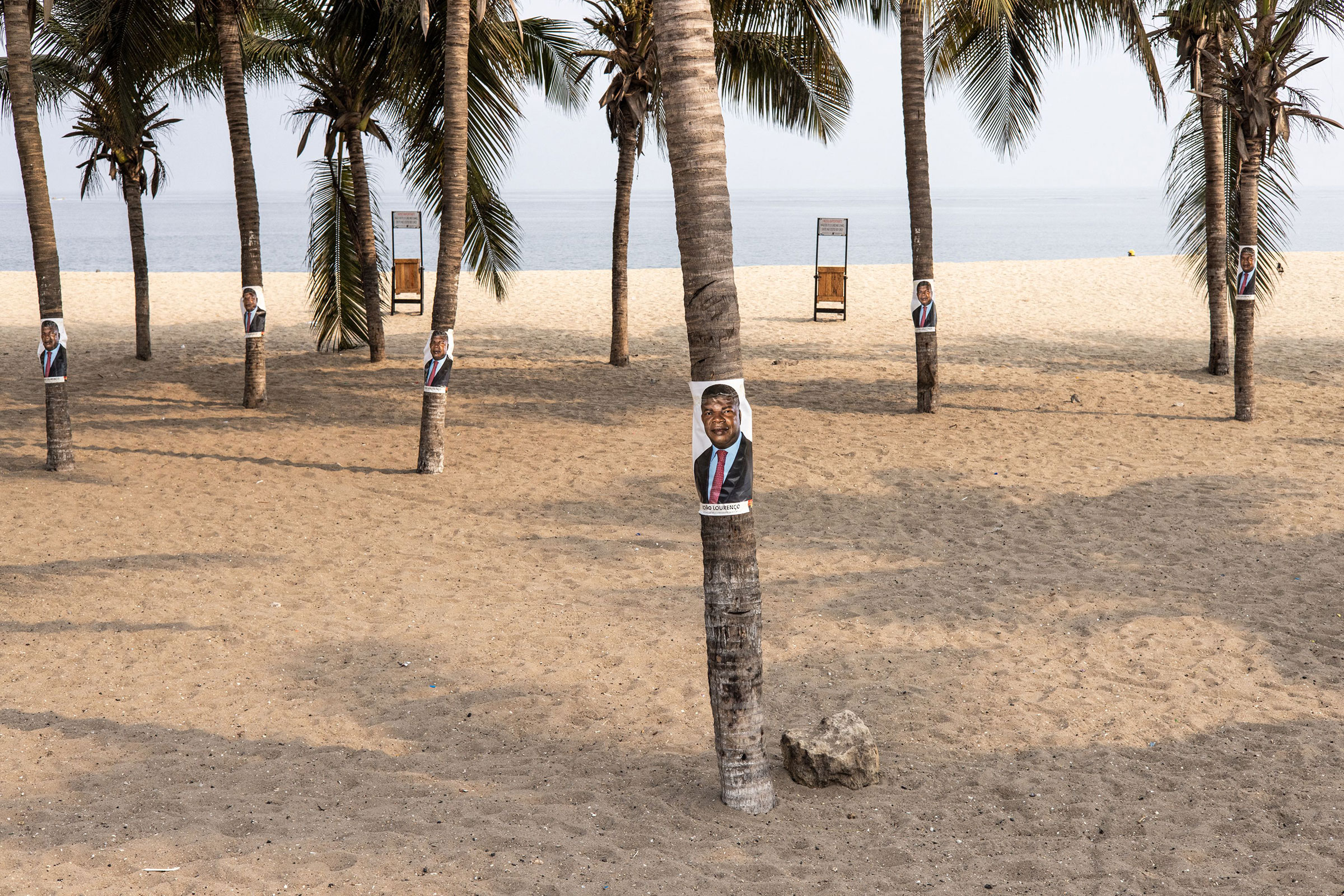 Campaign posters for the current President of Angola, Joao Lourenco, are pictured on palm trees along the beach front in Luanda on Aug. 23. (John Wessels—AFP/Getty Images)