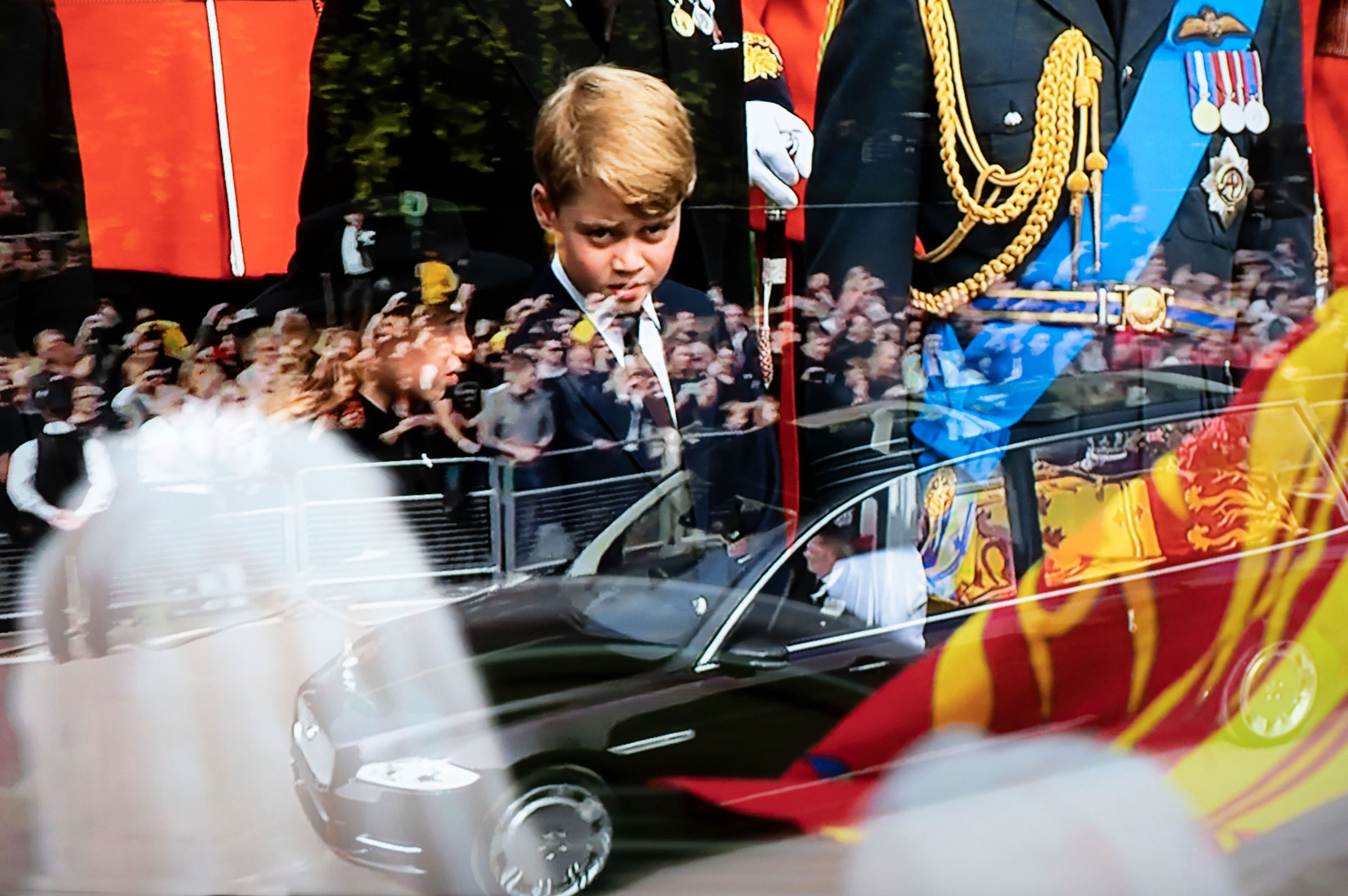 Photographed from a television broadcast, Queen Elizabeth's coffin in the State Hearse is driven to Windsor past crowds lining the road with Prince George, second in line to the throne, in the background. (Ian Berry—Magnum Photos)