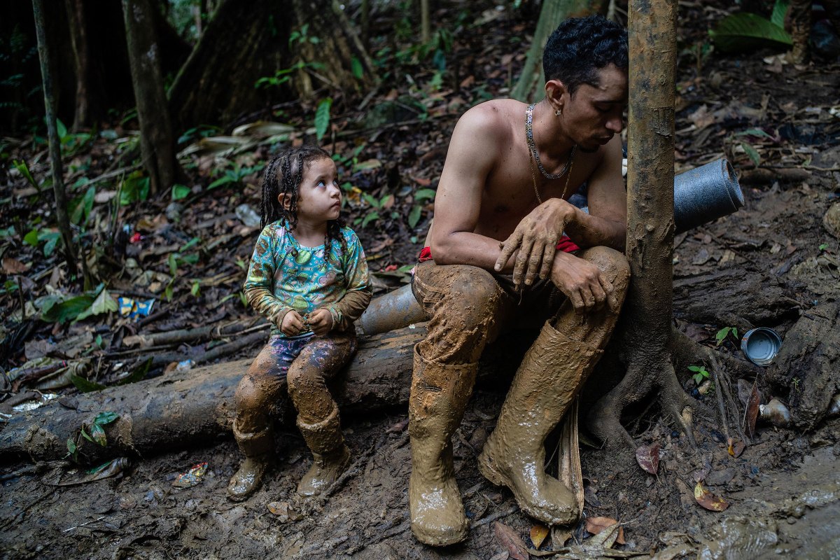 An exhausted man and child rest in the Darien Gap, with a week of walking still ahead across the 66-mile stretch of jungle terrain between Colombia and Panama, Sept. 23, 2022. Two crises are converging as record numbers of Venezuelans risk the deadly trek to reach the U.S. border: the economic and humanitarian disaster underway in South America and the bitter fight over immigration policy in Washington. (Federico Rios/The New York Times)