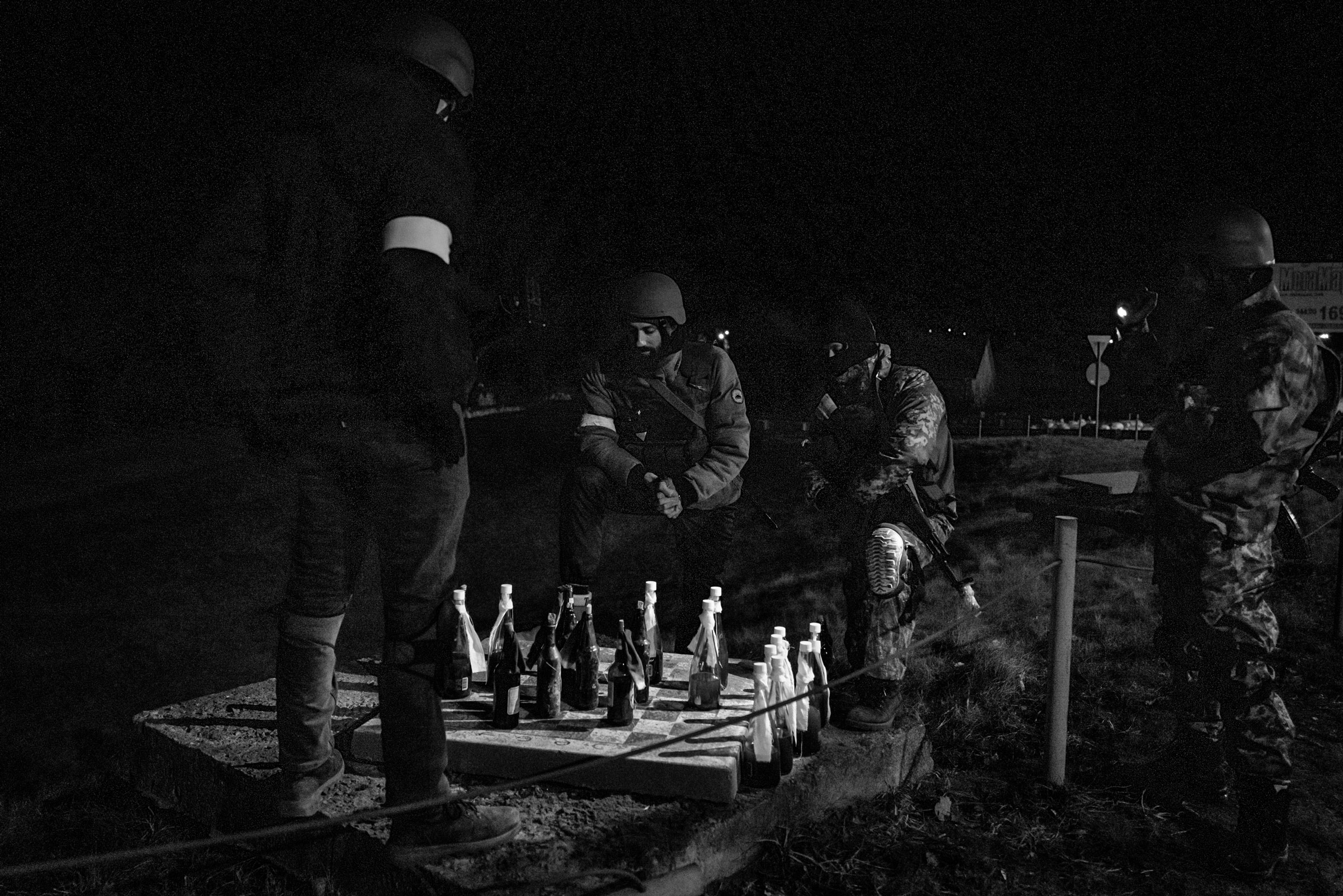 Members the Territorial Defense Forces who guard a large checkpoint briefly played a game of checkers with Molotov cocktails, as seen on the eastern outskirts of Kyiv, Ukraine, on March 5. With few vehicles passing because of the nighttime curfew, Territorial Defense members can have a moment of quiet while remaining on high alert for any suspicious activity. (Nicole Tung for Harper’s Magazine)