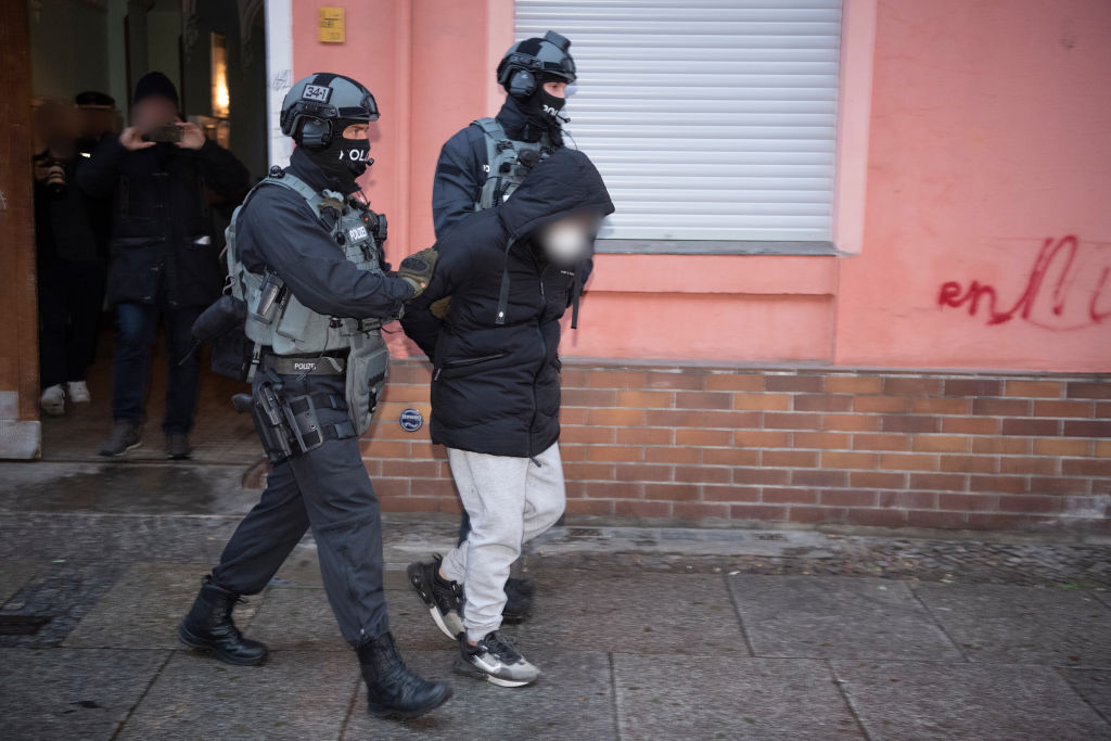 Police officers lead a man, pixelated for legal reasons, out of an apartment building in Schöneberg on Dec. 7, 2022. (Paul Zinken—picture alliance/Getty Images)