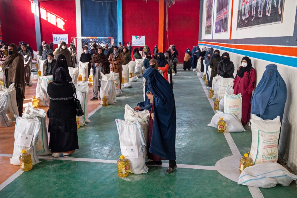 Afghan people stand with food aid being distributed by a non-governmental organization at a gymnasium in Kabul on Jan. 17, 2023. At least three leading international aid agencies have partially resumed life-saving work in Afghanistan, after assurances from the Taliban authorities that Afghan women can continue to work in the health sector. (Wakil Kohsar—AFP/Getty Images)