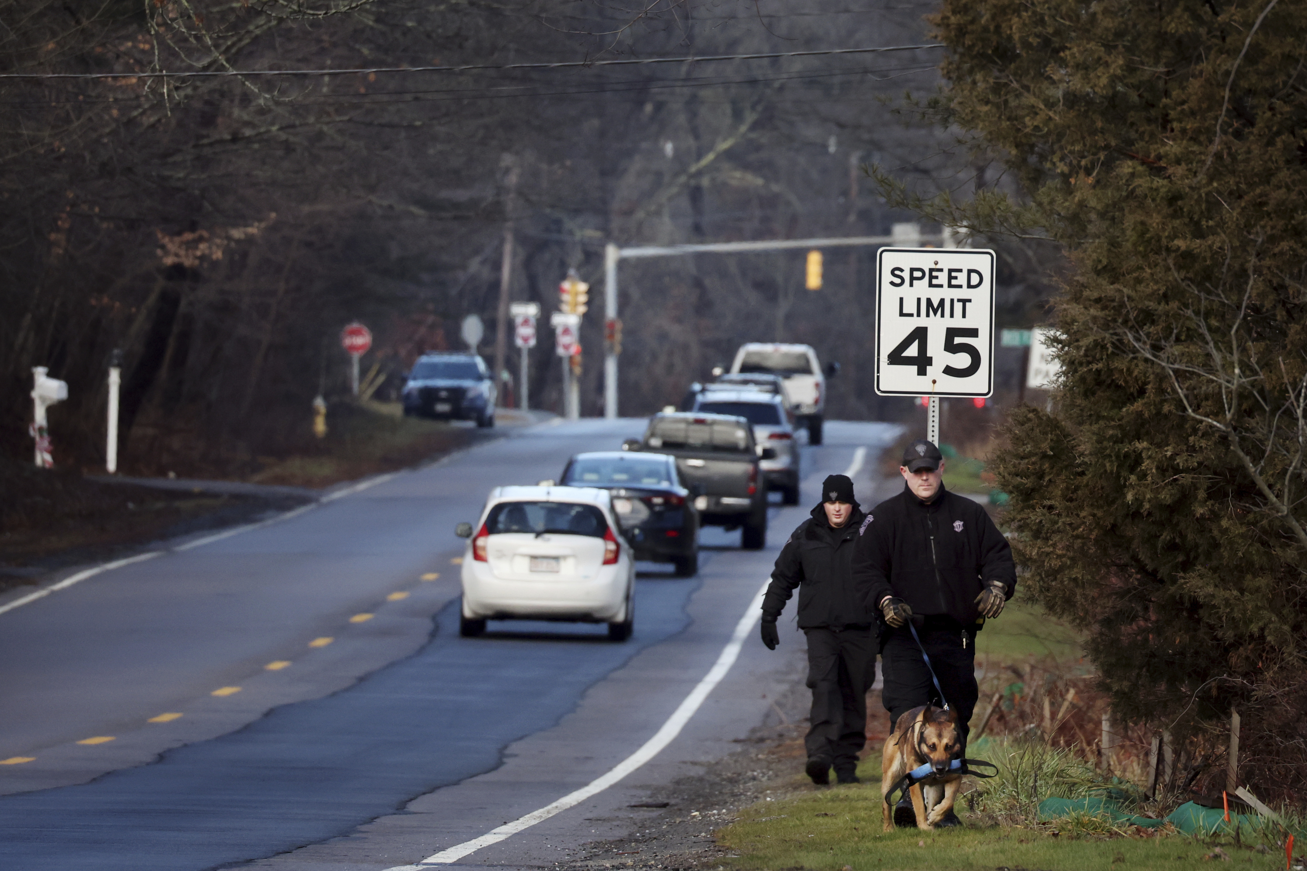 Members of a State Police K-9 unit search on Chief Justice Cushing Highway in Cohasset, Mass., Jan. 7, 2022. Authorities say the husband of a missing Massachusetts woman has been arrested for allegedly misleading investigators. Cohasset police and Massachusetts State Police on Sunday took Brian Walshe, 46, of Cohasset, Mass., into custody. His arrest comes after state and local police suspended their ground search for 39-year-old Ana Walshe, who has been missing since New Year’s Day. (Craig F. Walker/The Boston Globe via AP) (Craig F. Walker/The Boston Globe/AP)