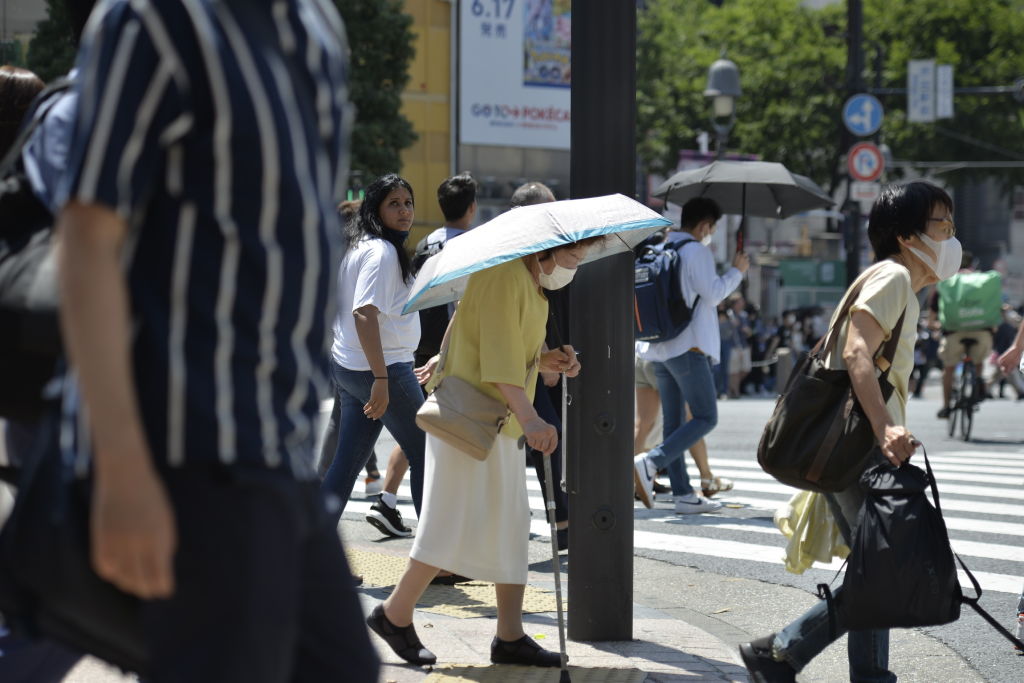 An older person walks on the street using an umbrella to protect herself from the sun on June 27, 2022, in the Shibuya district of Tokyo, Japan. (David Mareuil—Anadolu Agency/Getty Images)