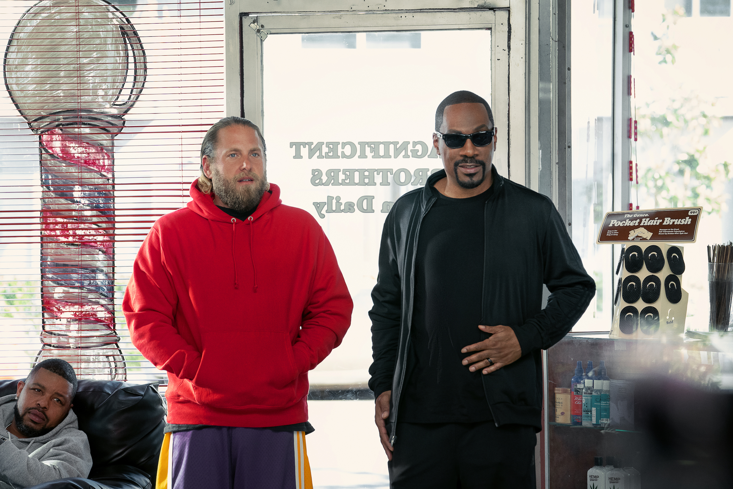 Jonah Hill's Ezra wearing a red hoodie in a Crip-territory barber shop to which Eddie Murphy's Akbar has brought him (Tyler Adams/Netflix)