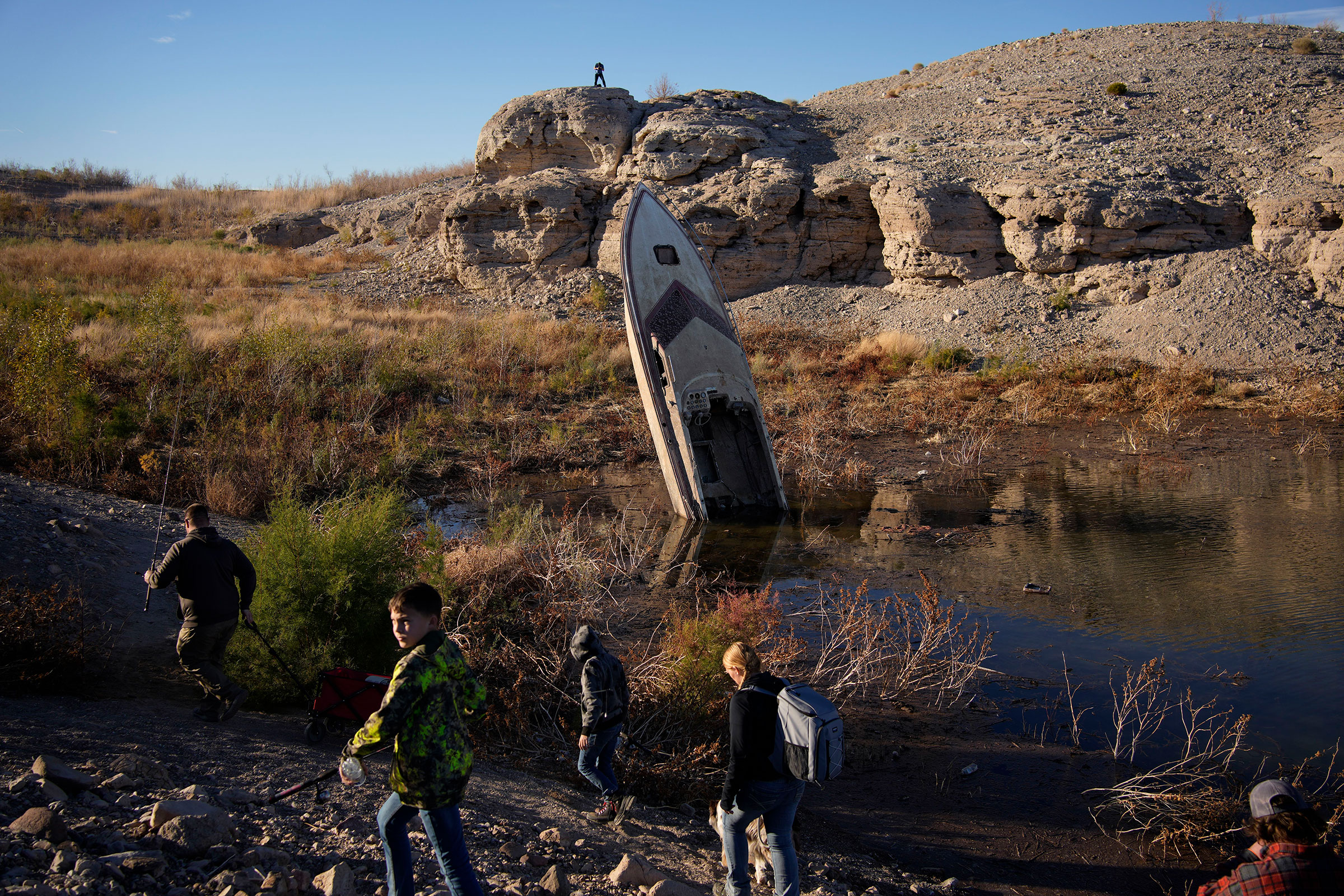 People walk by a formerly sunken boat standing upright into the air with its stern buried in the mud along the shoreline of Lake Mead at the Lake Mead National Recreation Area, Friday, Jan. 27, 2023, near Boulder City, Nev. (John Locher—AP)