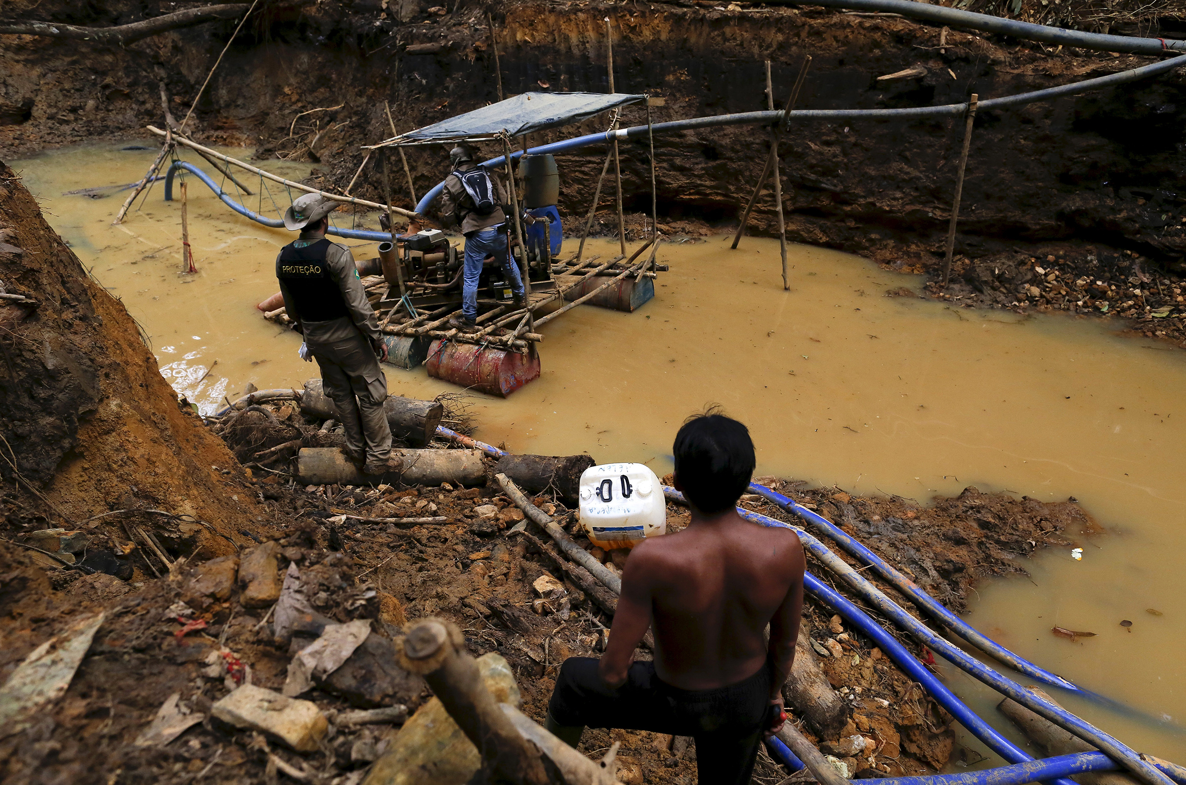 A Yanomami man, right, stands near an illegal gold mine on Indigenous land in the heart of the Amazon rainforest, in Roraima state, Brazil, in April 2016. Illegal miners continue to plague the area, sawing down trees and poisoning rivers with mercury in their lust for gold. (Bruno Kelly—Reuters)