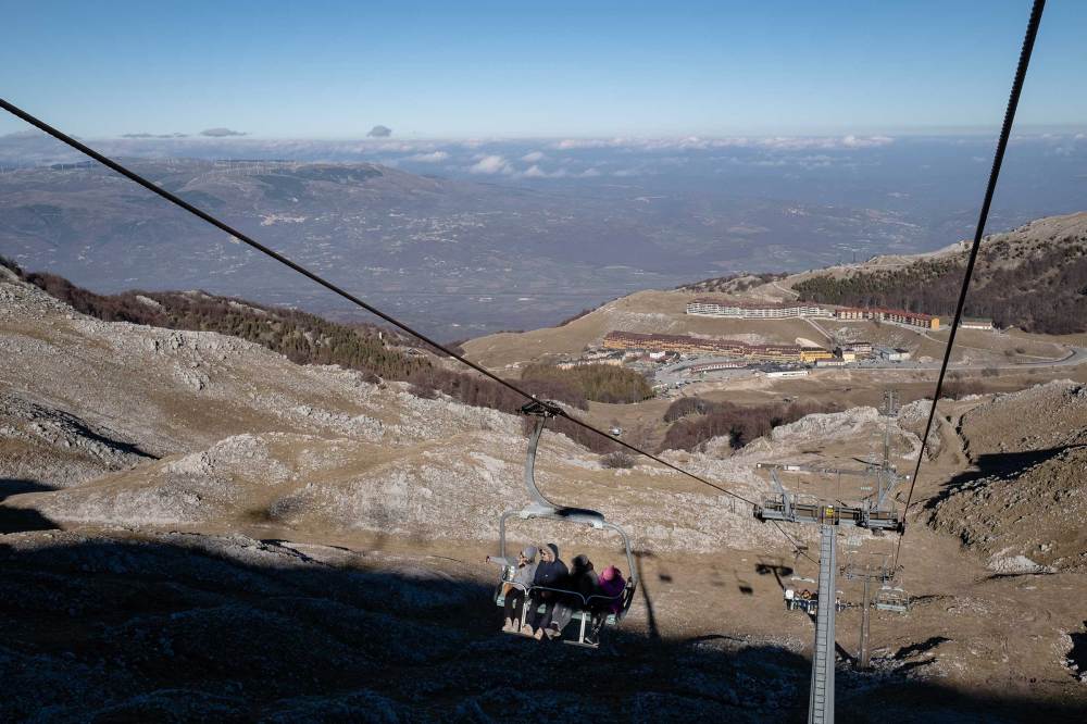 Visitors ride the chairlift to the top of a snowless Mount Miletto