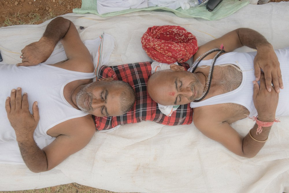 two men share a pillow while resting at a tent for the participants of Bharat Jodo Yatra