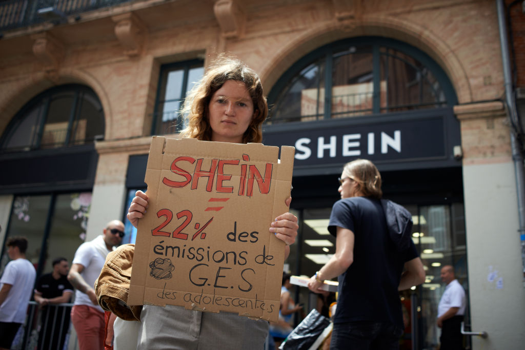 Bir Yok Olma İsyanı protestocusu elinde bir pankart okuyor "SHEIN = gençler için yayılan ısınma gazının %22'si" bir pop-up mağazasının önünde.  (Alain Pitton—NurPhoto/Getty Images)