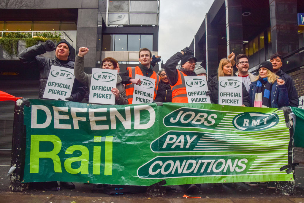 Rail, Maritime, and Transport (RMT) workers union members hold official picket placards behind a banner that states 'Defend rail jobs, pay, conditions' outside Euston Station in London on Jan. 4, 2022, as national rail strikes continue. (Vuk Valcic—SOPA/LightRocket/Getty Images)