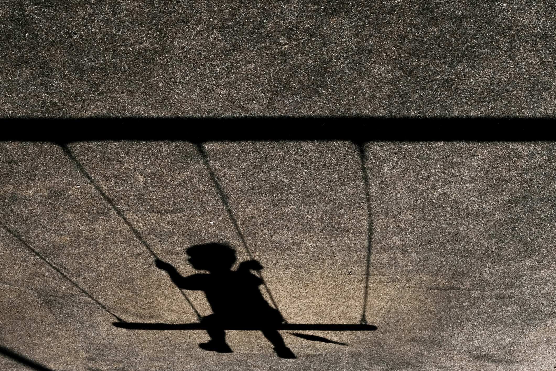 Horizontal shot of the shadow of a child on a swing on a grey wall