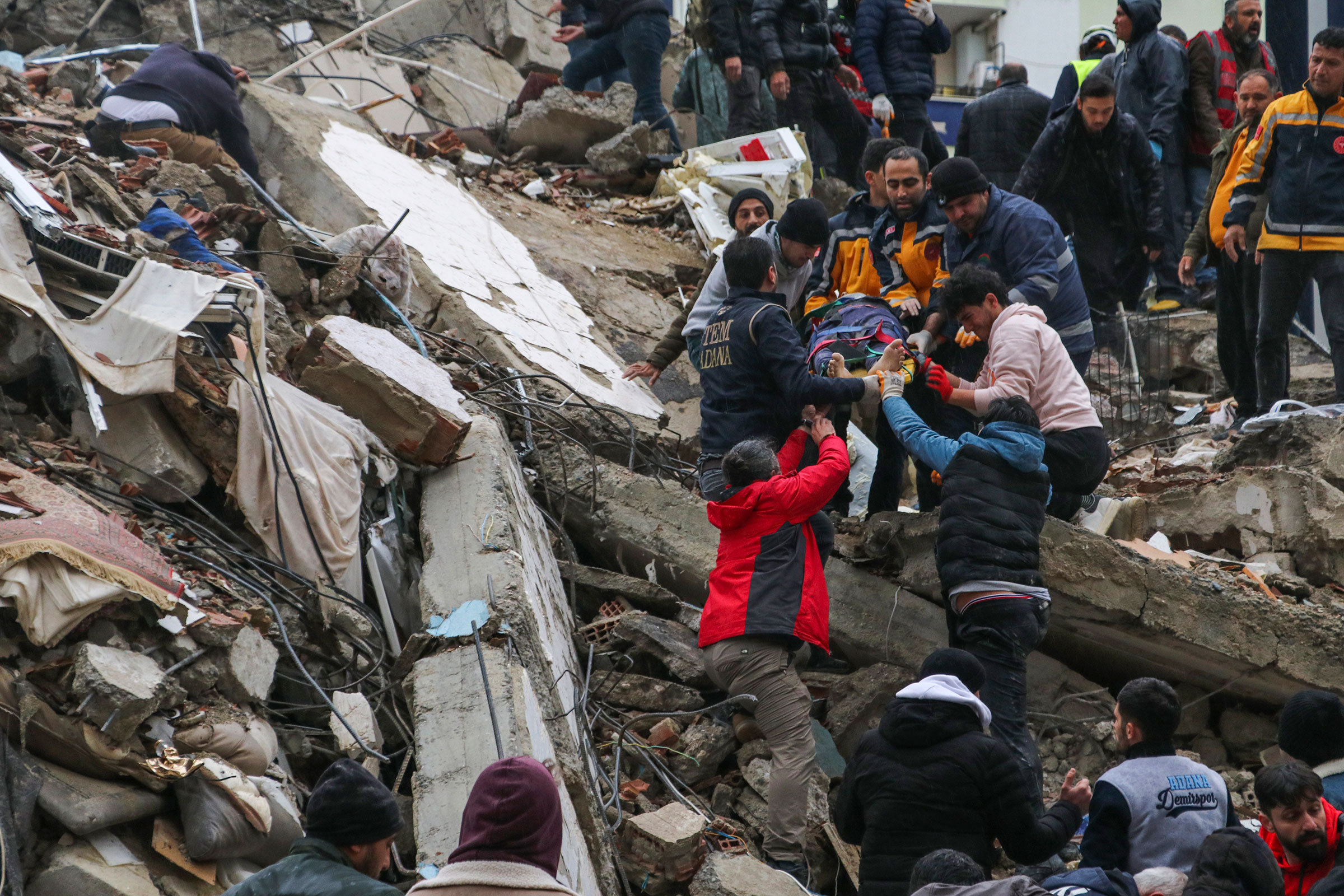 People and emergency teams rescue a person on a stretcher from a collapsed building in Adana, Turkey, on Feb. 6, 2023. A powerful quake has knocked down multiple buildings in southeast Turkey and Syria and many casualties are feared. (IHA agency/AP)
