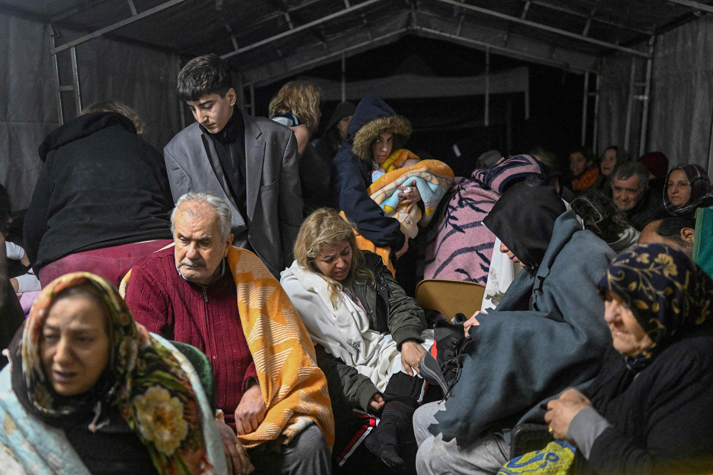 Earthquake survivors sit sheltering in a tent in Hatay, the day after a 7.8-magnitude earthquake struck the country's southeast, on Feb. 7, 2023. (Bulent Kilic—AFP/Getty Images)