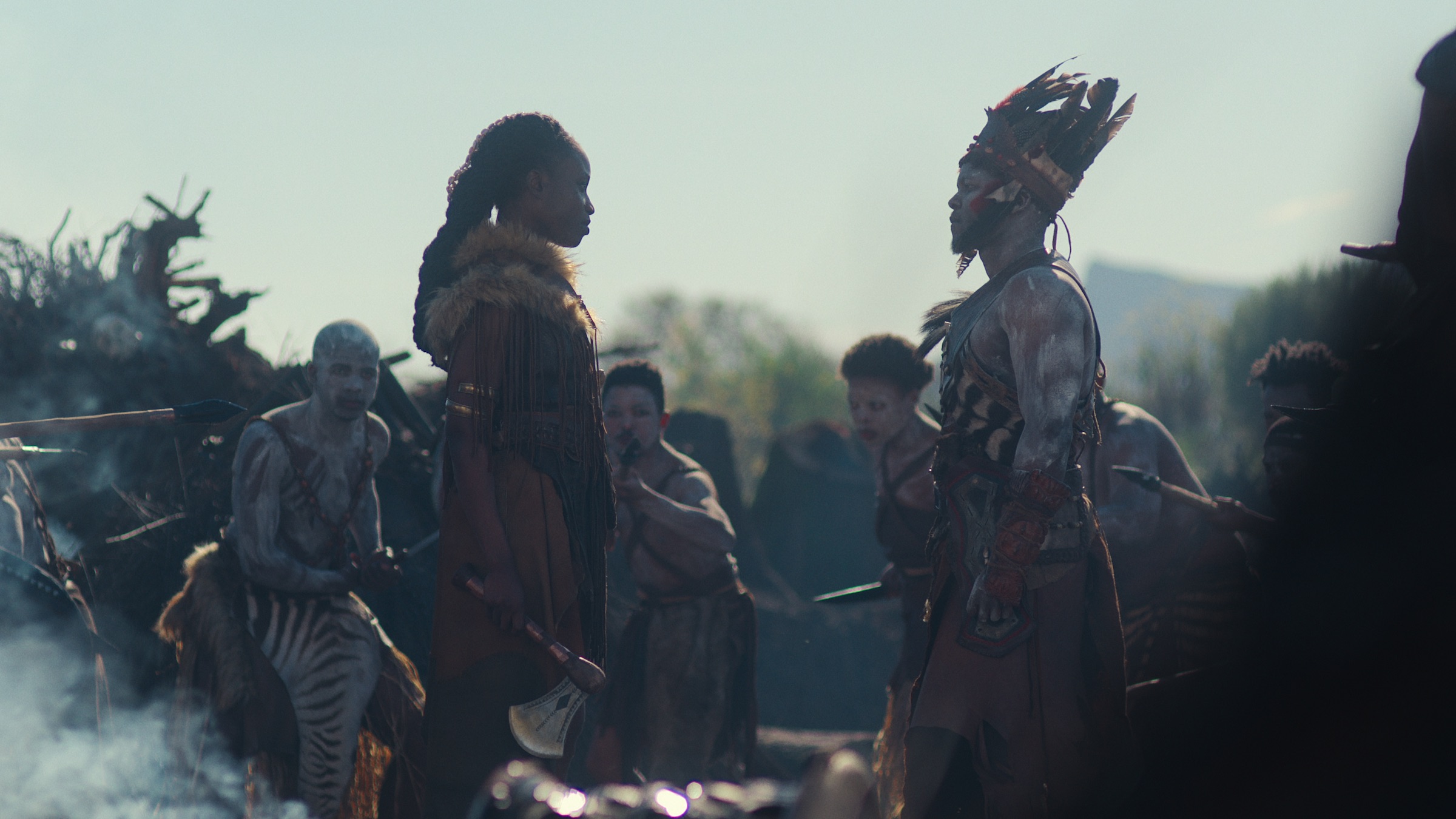 Njinga and Kasa stare at each other, face-to-face, surrounded by Imbangala warriors with weapons drawn.