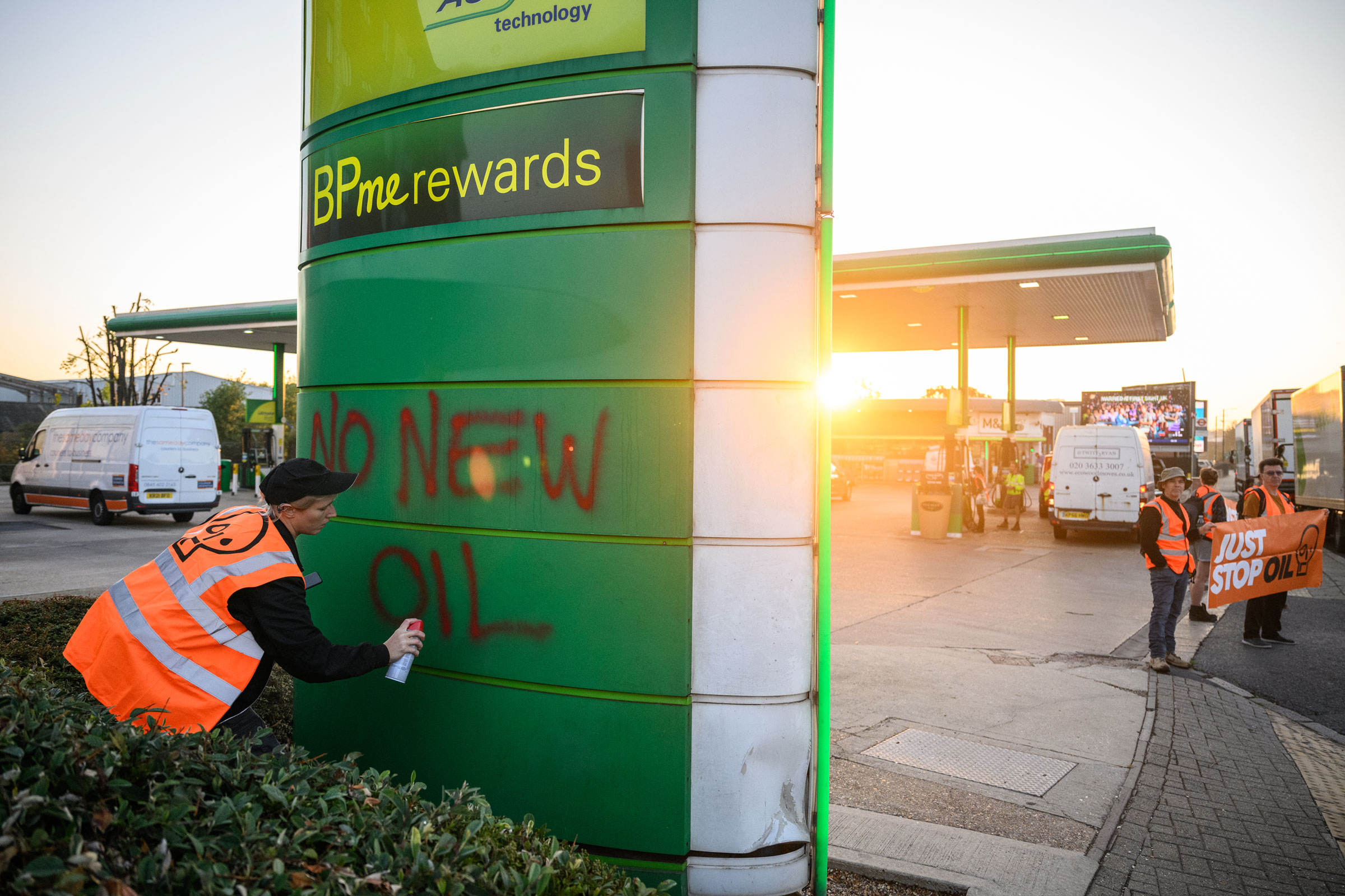 A woman sprays a message reading “No New Oil” on a sign outside a BP petrol station