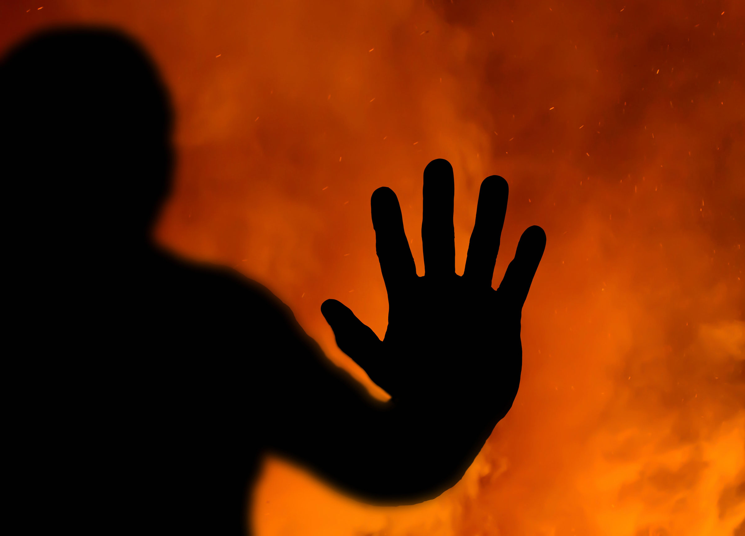 Abstract of a silhouette of the hand pressed up against the inside of a window with a fire raging in the background
