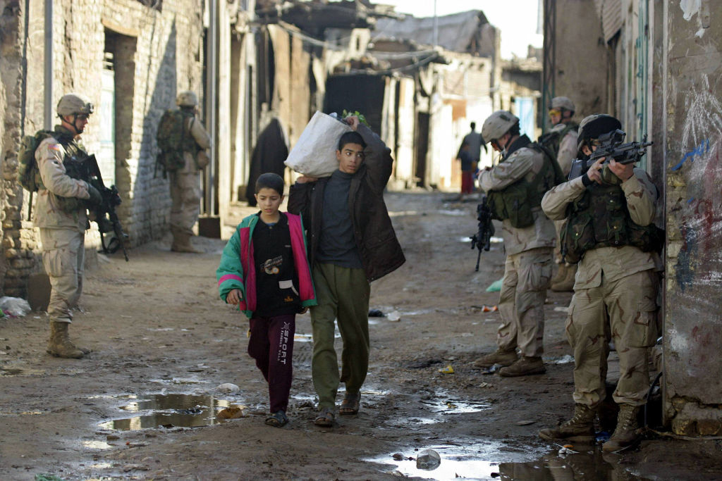 Iraqi boys walk between US soldiers patroling an alley in the notorious Haifa street district, a haven for the insurgency in central Baghdad, 23 January 2005. (CHRISTOPHE SIMON-AFP)