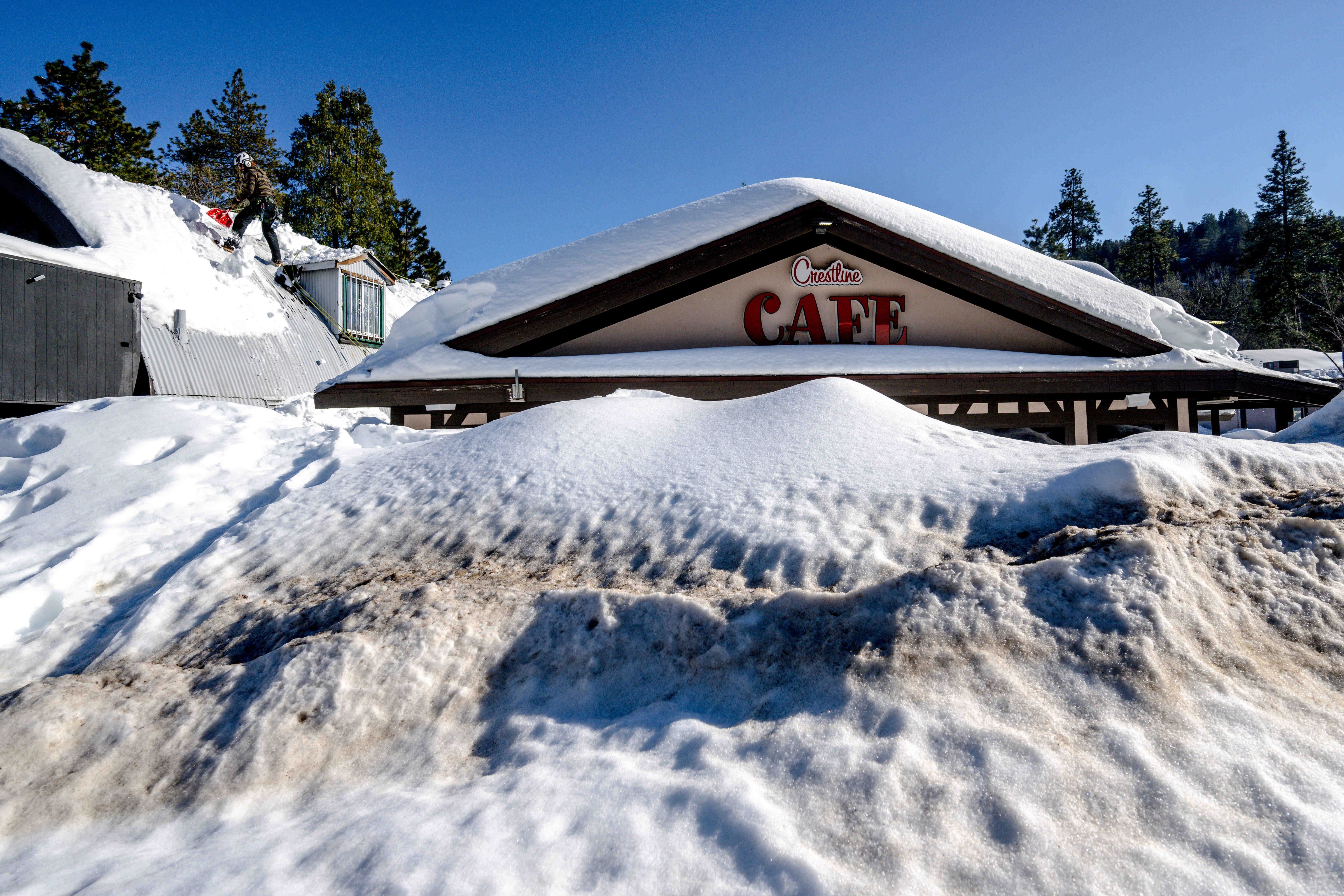 A man shovels snow off the roof of a store in Crestline on Friday, March 3, 2023, as buildings remain buried in several feet of snow from recent winter storms. (Watchara Phomicinda–MediaNews Group/The Press-Enterprise/Getty Images)