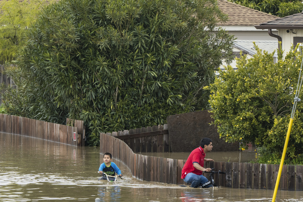 A boy and a man ride bicycles through floodwaters in Watsonville, Calif., on March 11, 2023. (Nic Coury—AP)