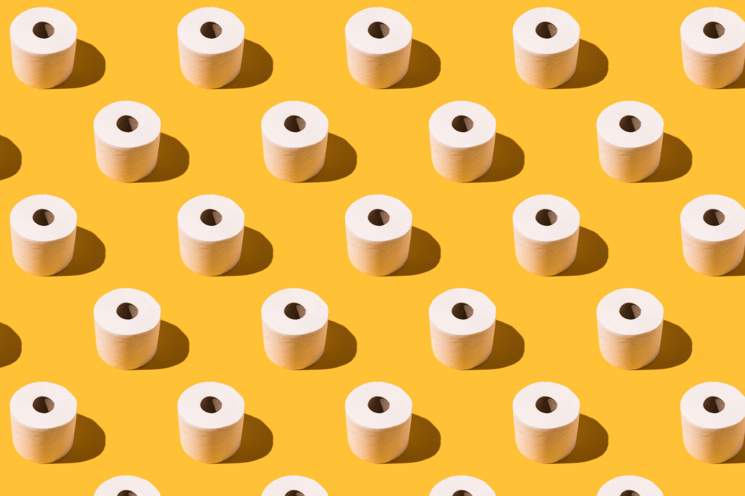 Pattern of white toilet paper rolls on yellow background. Concept of going to the bathroom, cleaning and pooping and peeing.