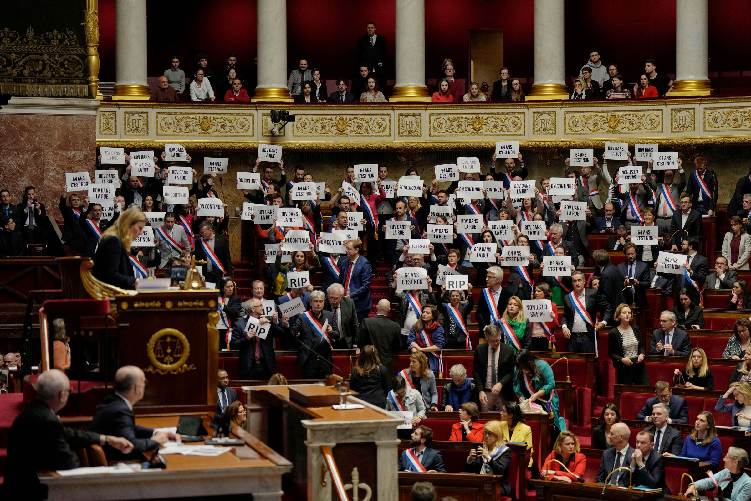 Far-left lawmakers react as they hold papers reading: “64 years. It is no,” at the National Assembly in Paris on March 20, 2023.