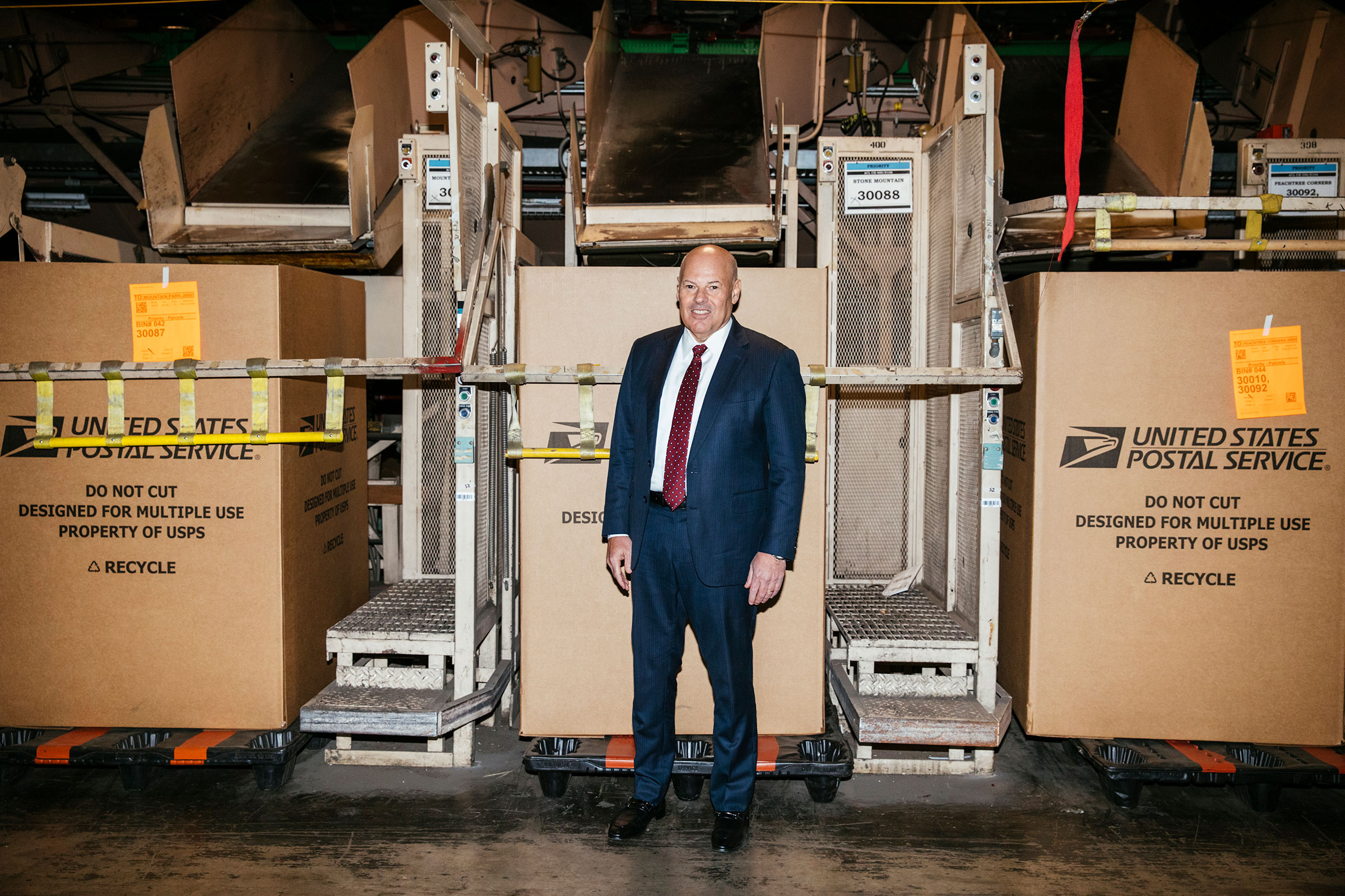 United States Postmaster General Louis DeJoy plans to modernize the outdated postal system. He poses for a portrait in front of a parcel sorting machine at the USPS Atlanta Network Distribution Center in Atlanta, Georgia February 3, 2023. Photo by Kendrick Brinson