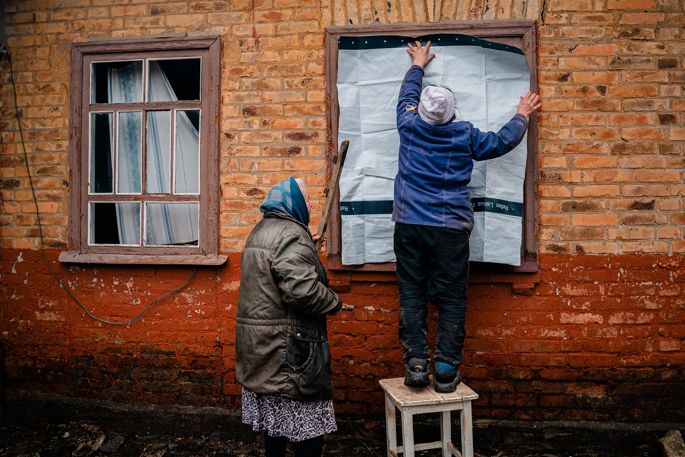 Elderly women placard a plastic sheet over a broken window after shelling in Chasiv Yar, near Bakhmut on Feb. 28 amid Russia's military invasion on Ukraine. (Dimitar Dilkoff—AFP/Getty Images)