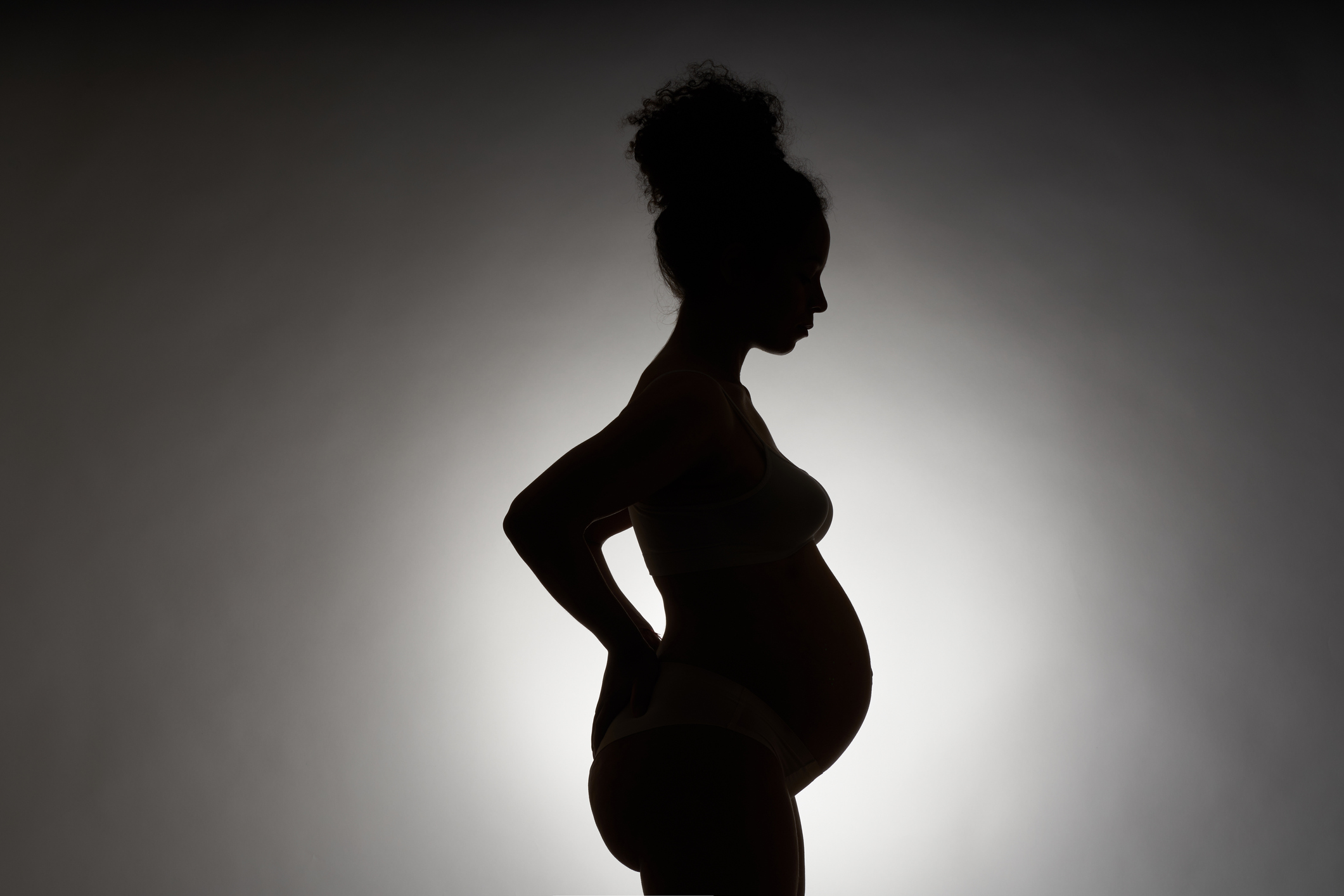 Silhouette of a pregnant African-American woman on a white background. The profile of a young woman with curly hair in a bump stands and holds her hands on her back. The concept of motherhood, pregnancy, back pain and childbirth.
