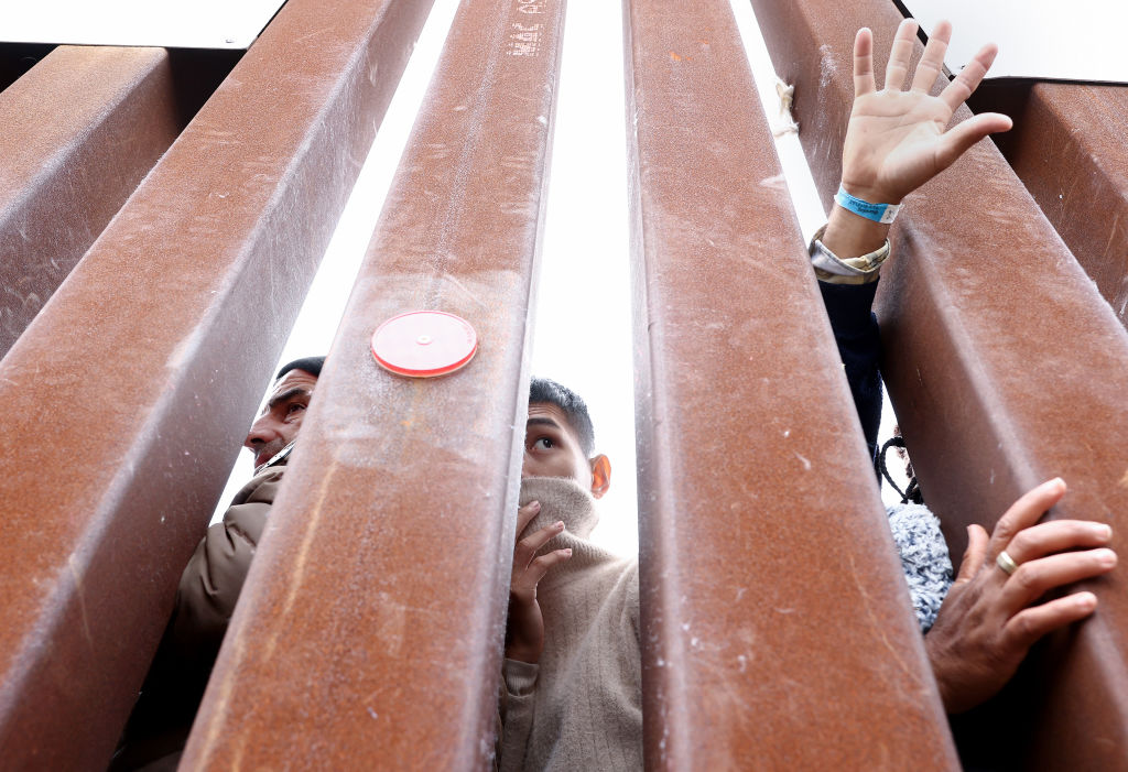 Immigrants stuck in a makeshift camp between the U.S. and Mexico look through the border wall as volunteers offer assistance on the other side on May 13, 2023 in San Diego, California. (Mario Tama—Getty Images)