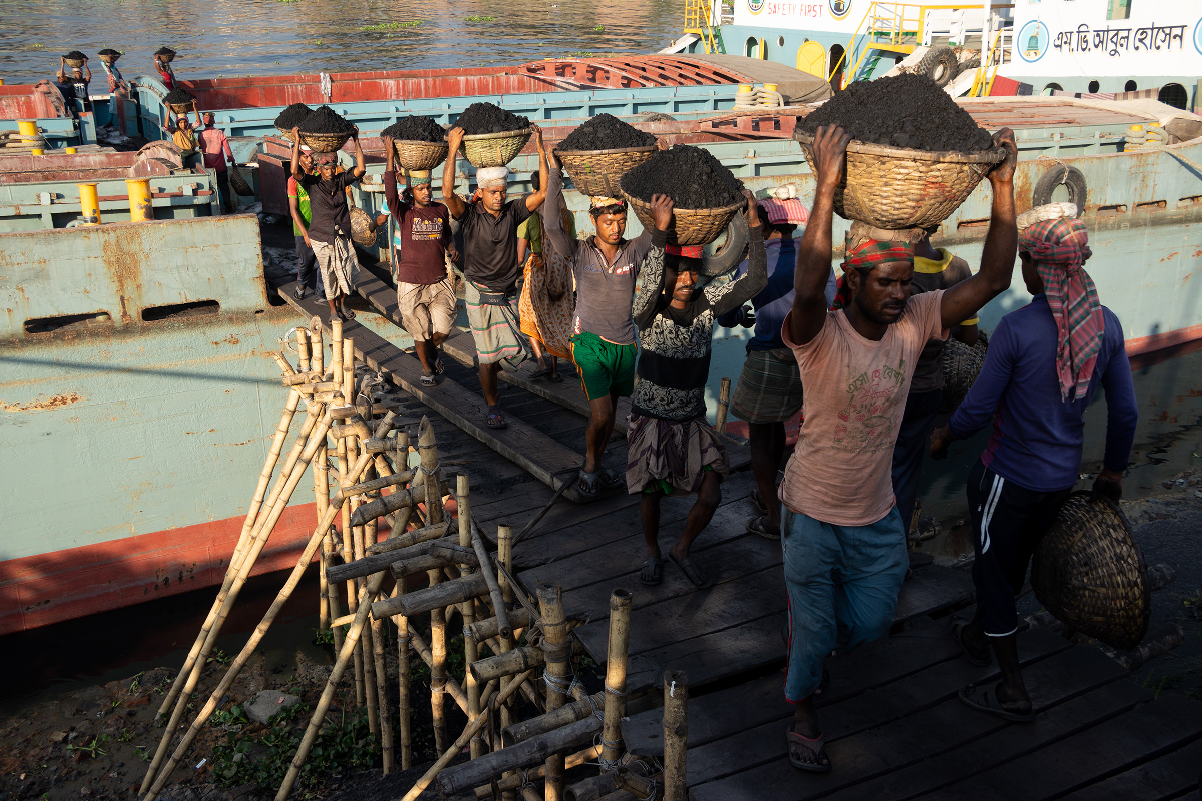 İşçiler, 12 Ocak'ta Bangladeş'in Dhaka kentinde bir kargo gemisinden kömürü boşaltırken başlarının üstünde kömür dolu sepetler taşıyorlar. Gündelik işçiler, gemiden boşaltılan her 30 sepet kömür için yaklaşık 1 dolar kazanıyor.  Kavurucu güneş altında uzun çalışma saatleri, yoğun toz birikimi ve aşırı yük taşıma, çalışanlar için ciddi sağlık tehlikeleri oluşturmaktadır.  (Joy Saha—Shutterstock)