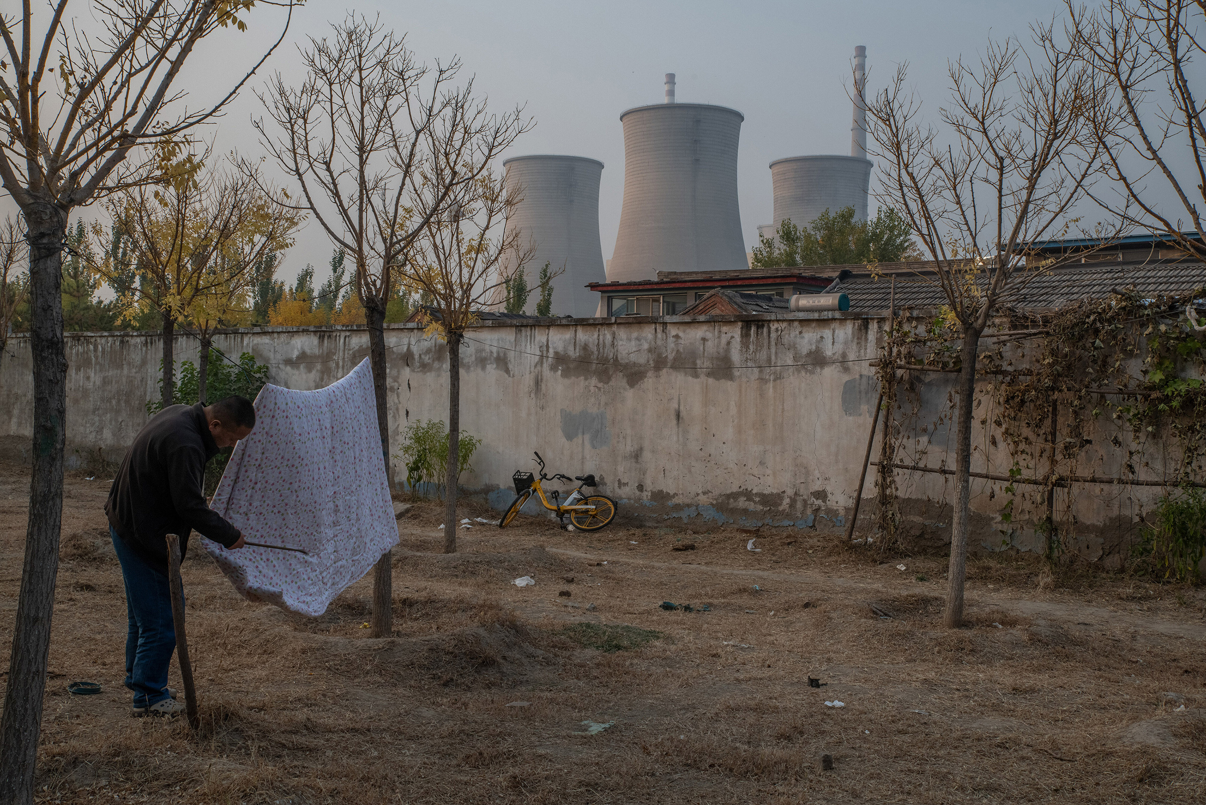 25 Ekim 2022'de Pekin'de kömürle çalışan bir elektrik santralinin yanında yorganın tozunu silken bir adam. (Gilles Sabrié—The New York Times/Redux)