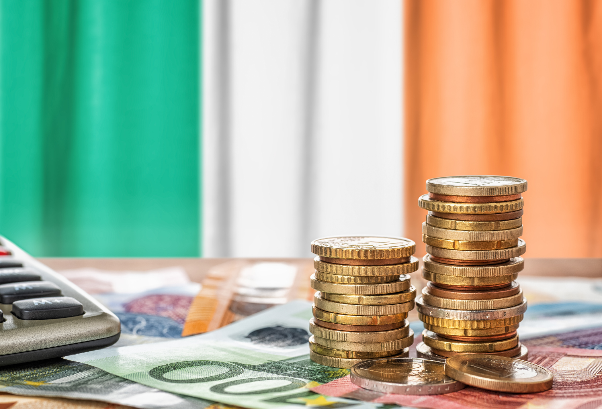 Euro banknotes and coins in front of the national flag of Ireland