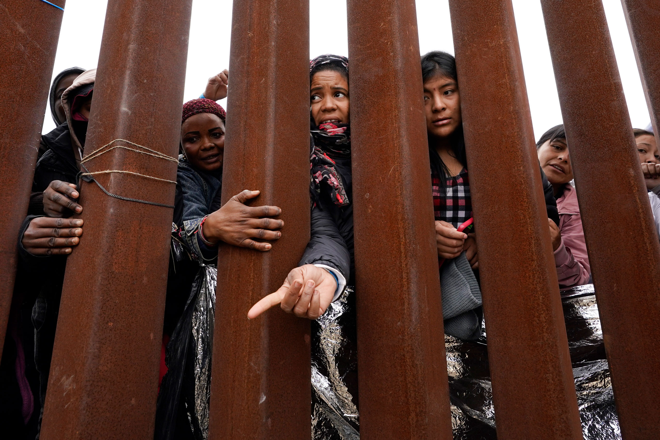 Migrants reach through a border wall for clothing handed out by volunteers, as they wait between two border walls to apply for asylum in San Diego, Calif., on May 12, 2023. (Gregory Bull—AP)