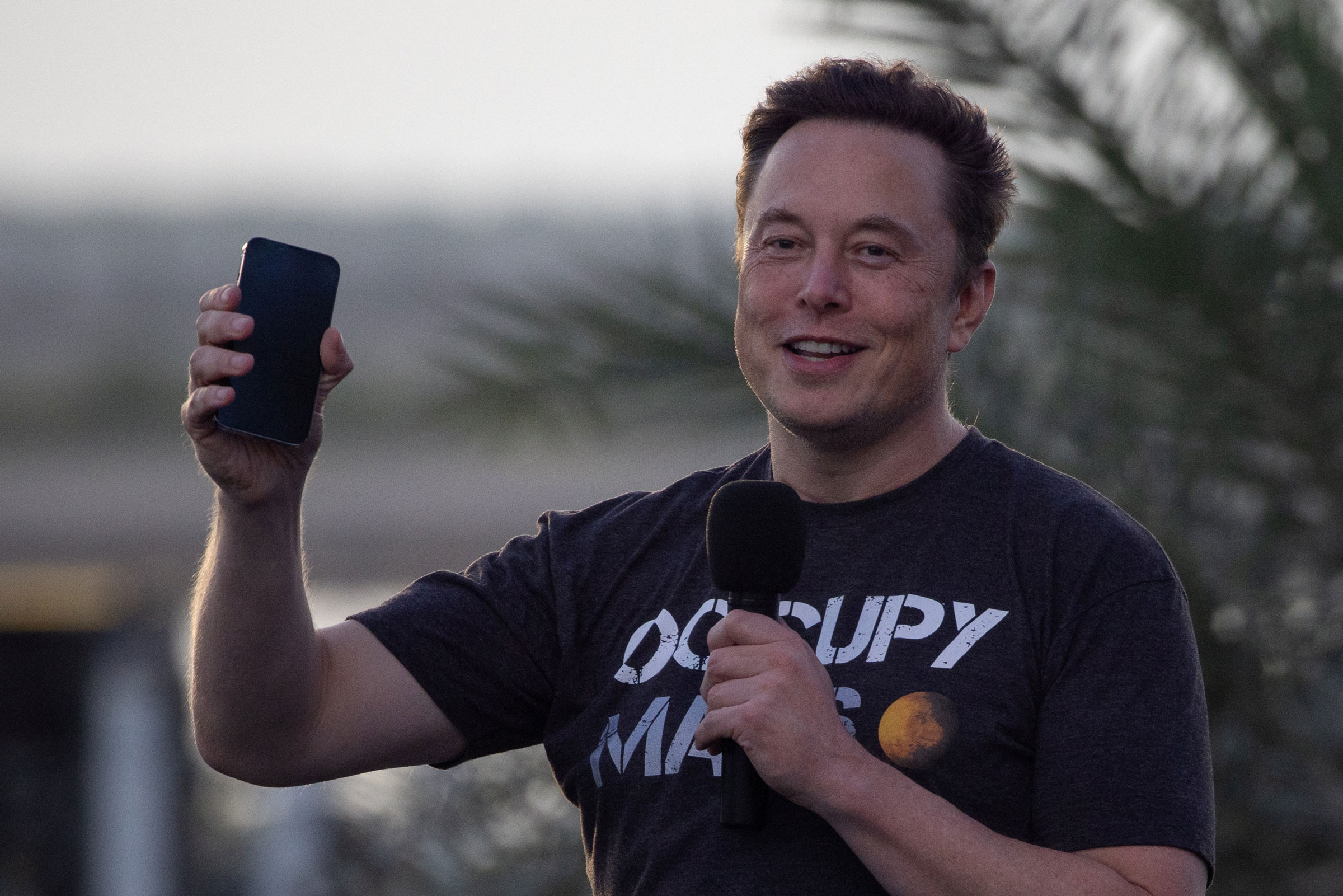 Elon Musk raises his phone during a news conference at the SpaceX Starbase