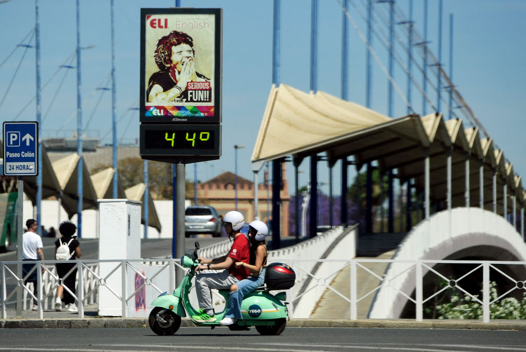 A couple ride a Vespa motorcycle past a street thermometer reading 44 degrees Celsius in Seville on April 26, 2023 as Spain is bracing for an early heat wave.