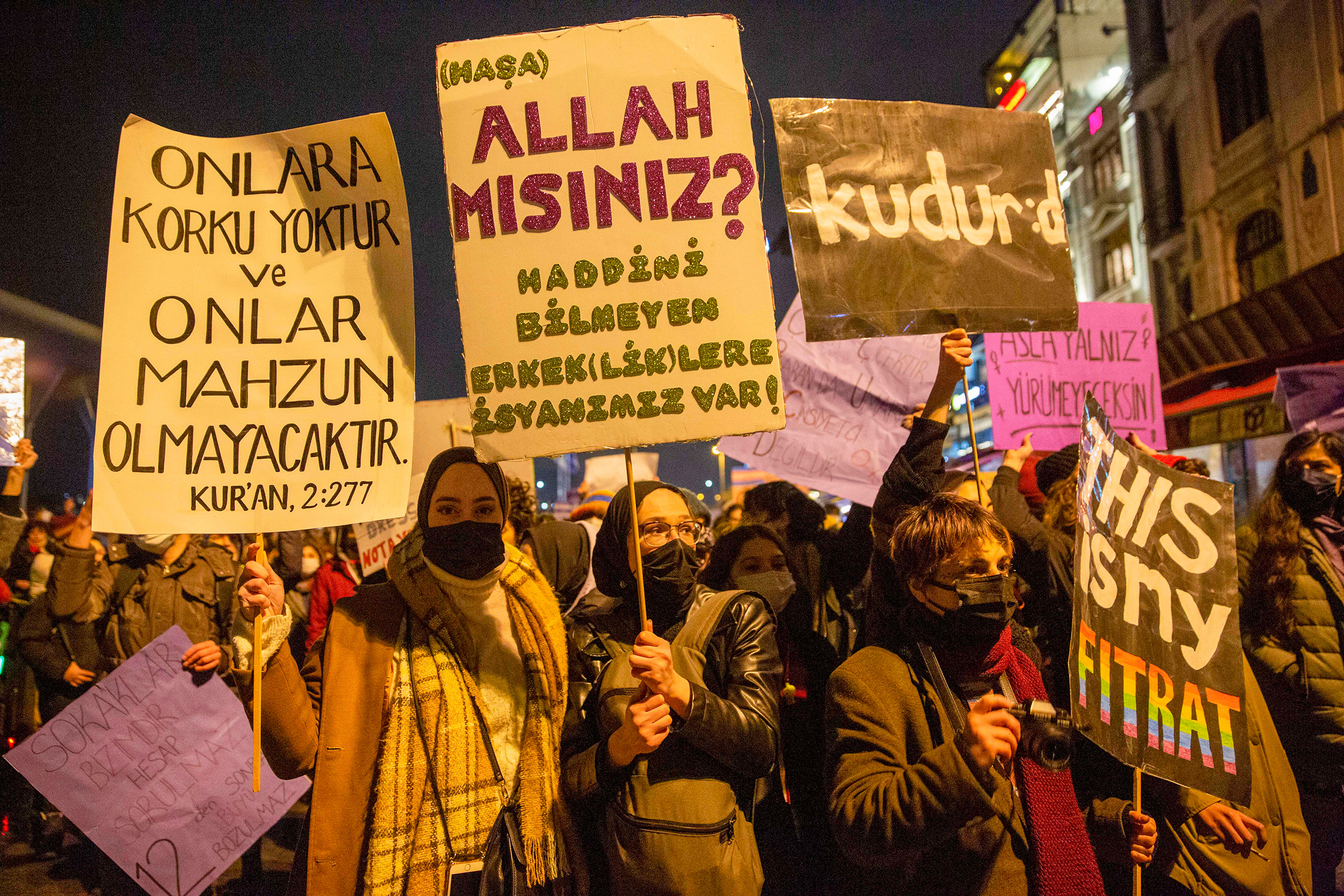Women hold posters reading, “Are you God? We’re rebelling against unrestrained men and masculinity,” and, “On them shall be no fear, nor shall they grieve, Quran verse 2:277,” at a feminist night march on March 8, 2022. (Özge Sebzeci for the Fuller Project)