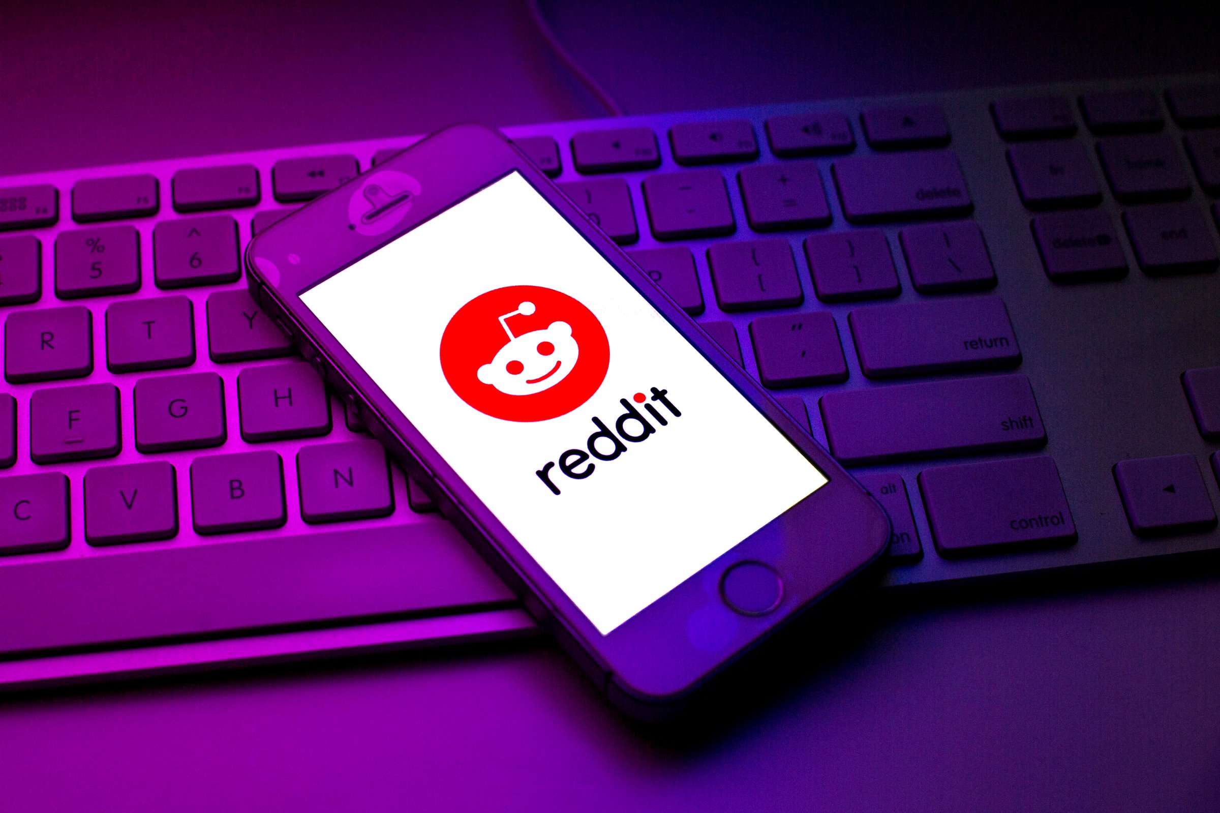Reddit logo seen displayed on a smartphone on top of a computer keyboard.