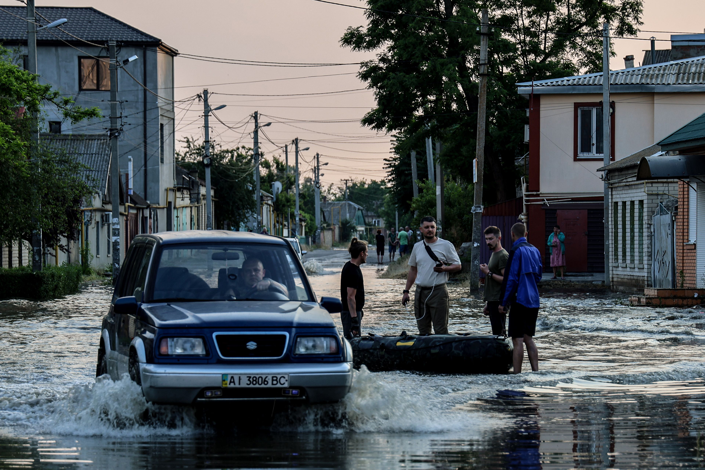 A car makes its way past people standing next to an inflatable boat, in a flooded street of Kherson on June 6. (Ivan Antypenko—EPA-EFE/Shutterstock)