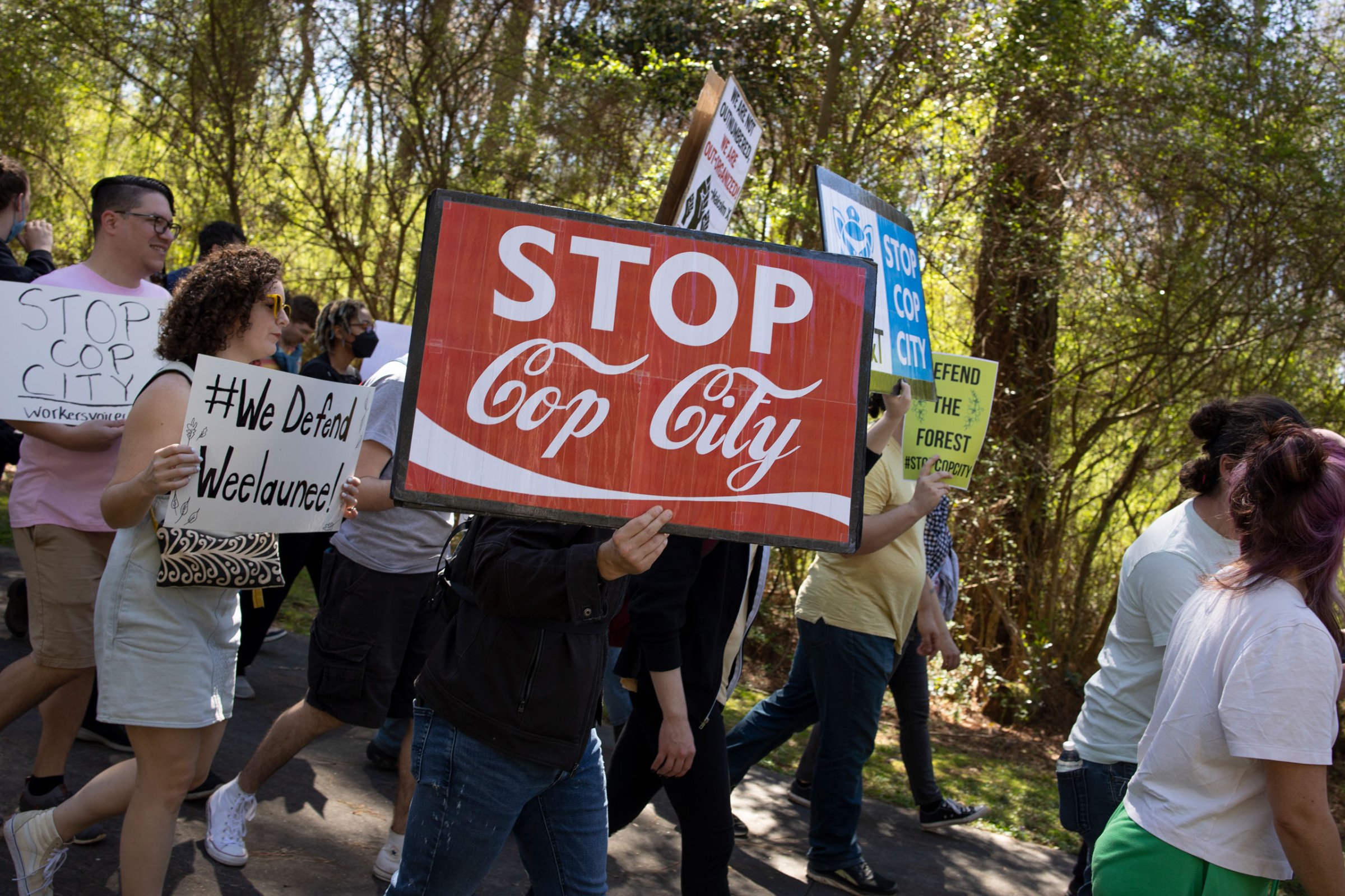 Activists march through a forest holding signs protesting the Cop City development