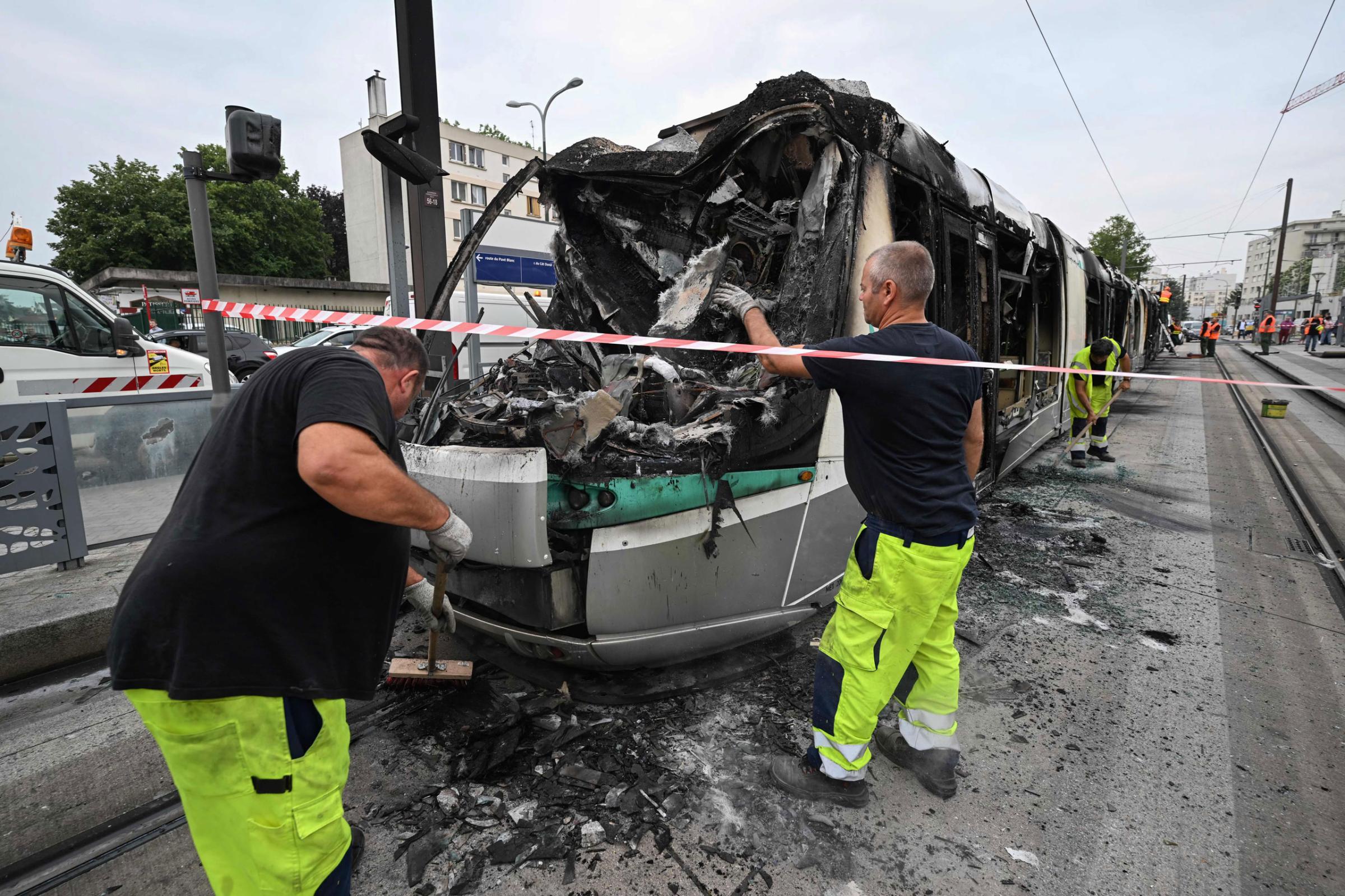 Workers clean up the debris of a burnt tram destroyed during protests the previous night in Clamart, southwest of Paris