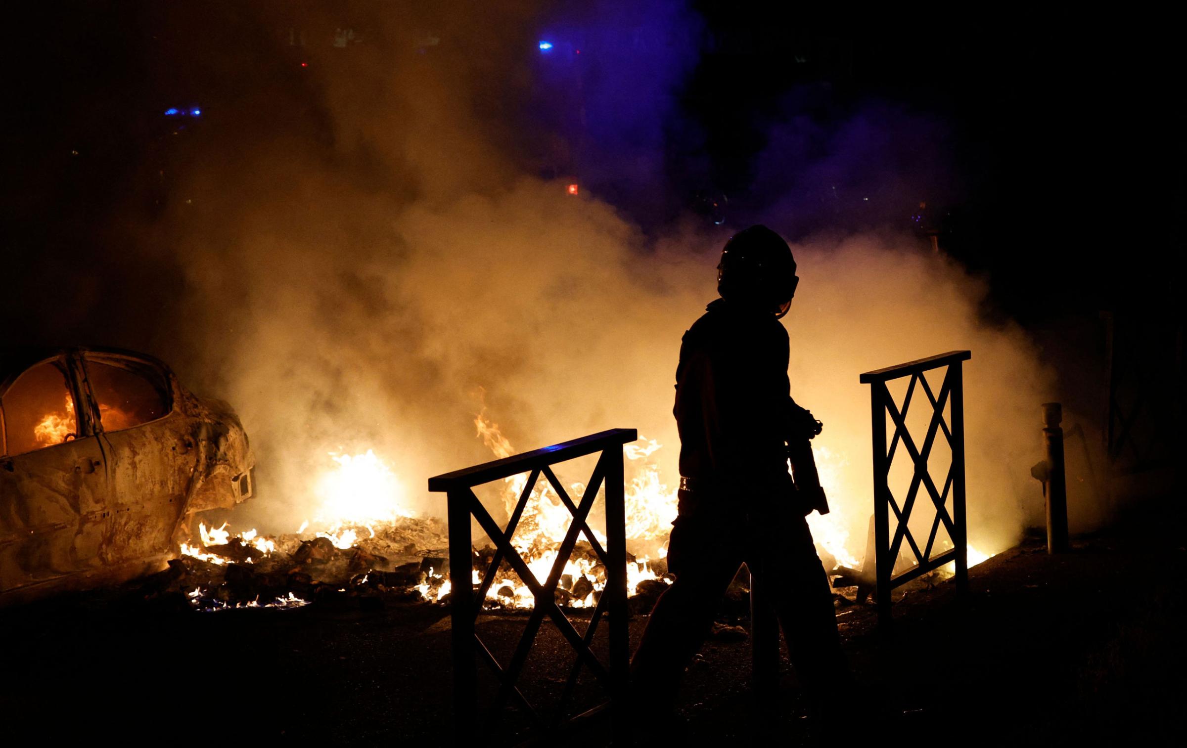 A firefighter extinguishes the flames of a car set on fire during protests in Nanterre