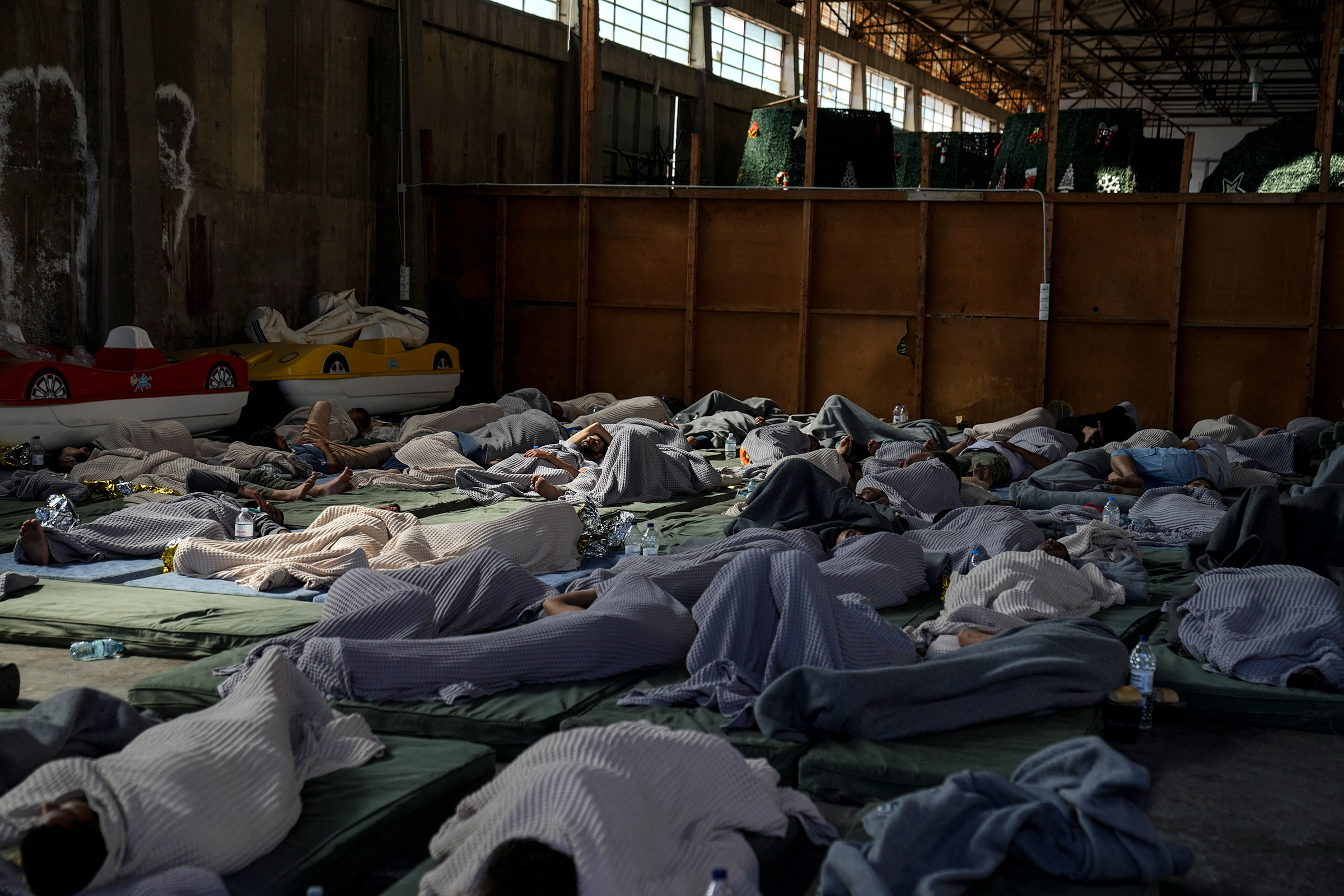 Survivors of a shipwreck sleep at a warehouse at a port in Greece