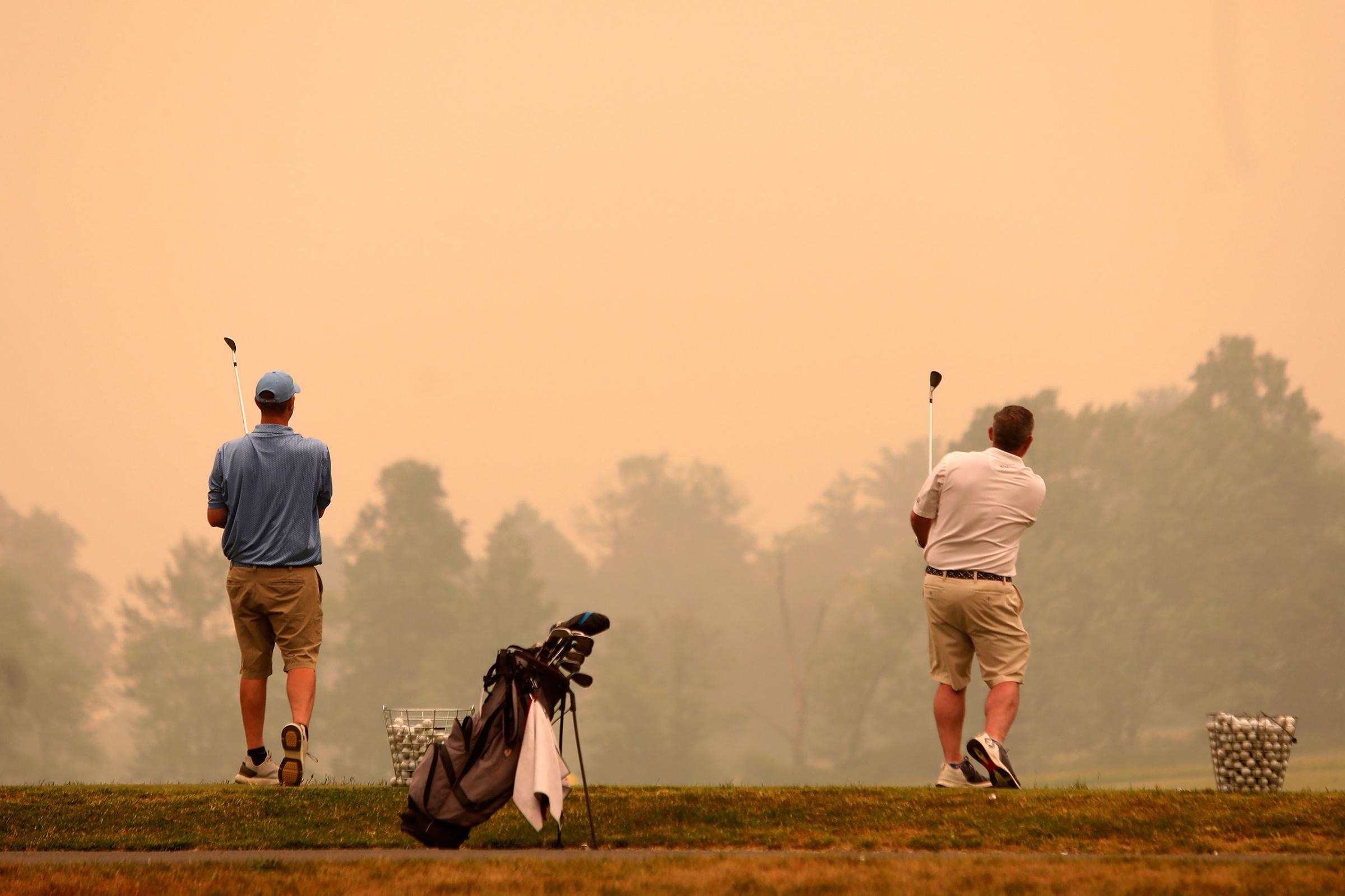Golfers watch their shots at the driving range at Valley Country Club in Sugarloaf, Pa., as smoke from wildfires in Canada fill the air