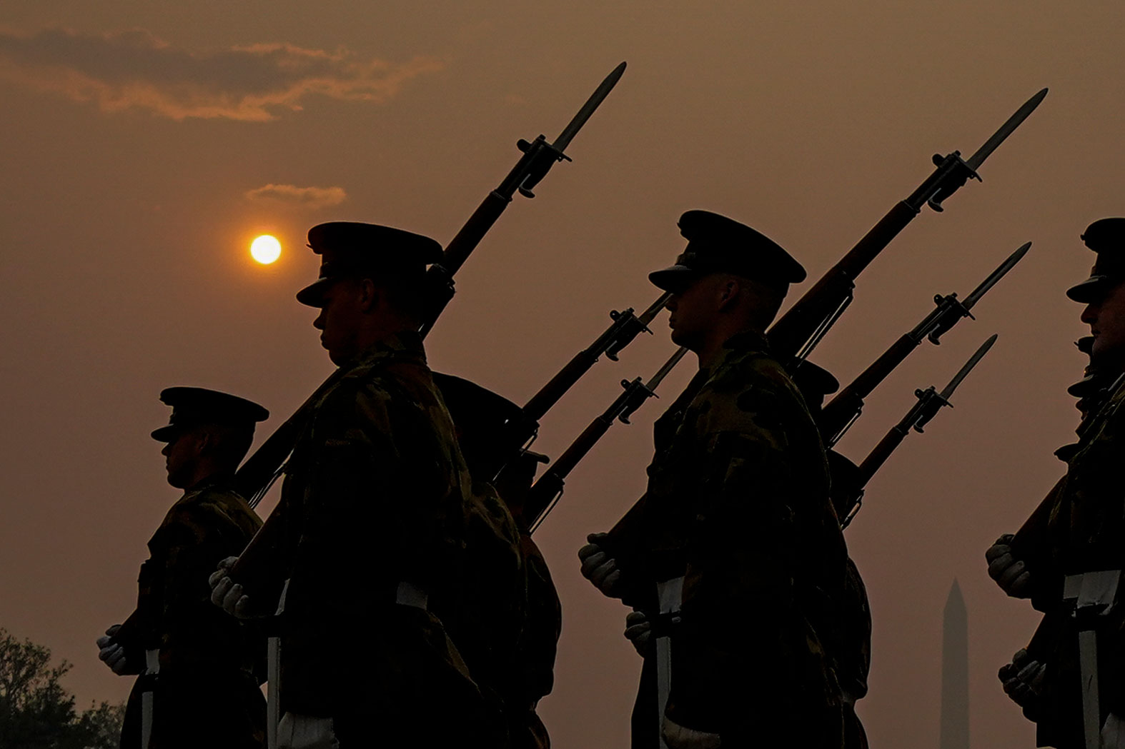 Members of the Marine Corps honor color guard rehearse near the Reflecting Pool with the sun rising over a thick layer of smoke