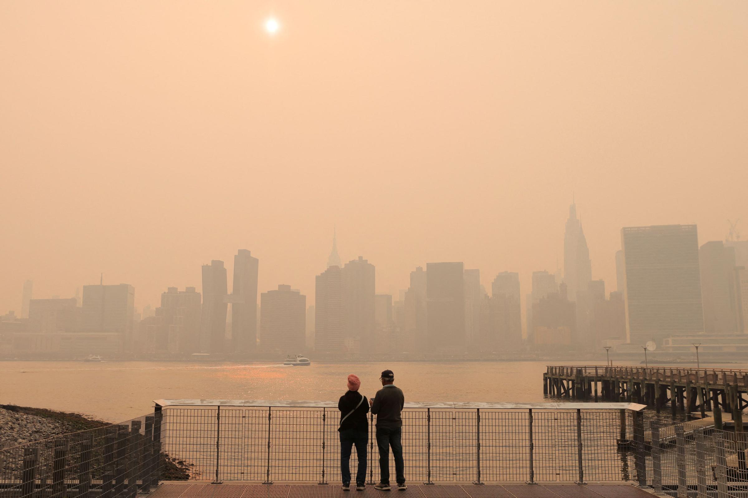 People watch the sunset as haze and smoke caused by wildfires in Canada hang over the Manhattan skyline