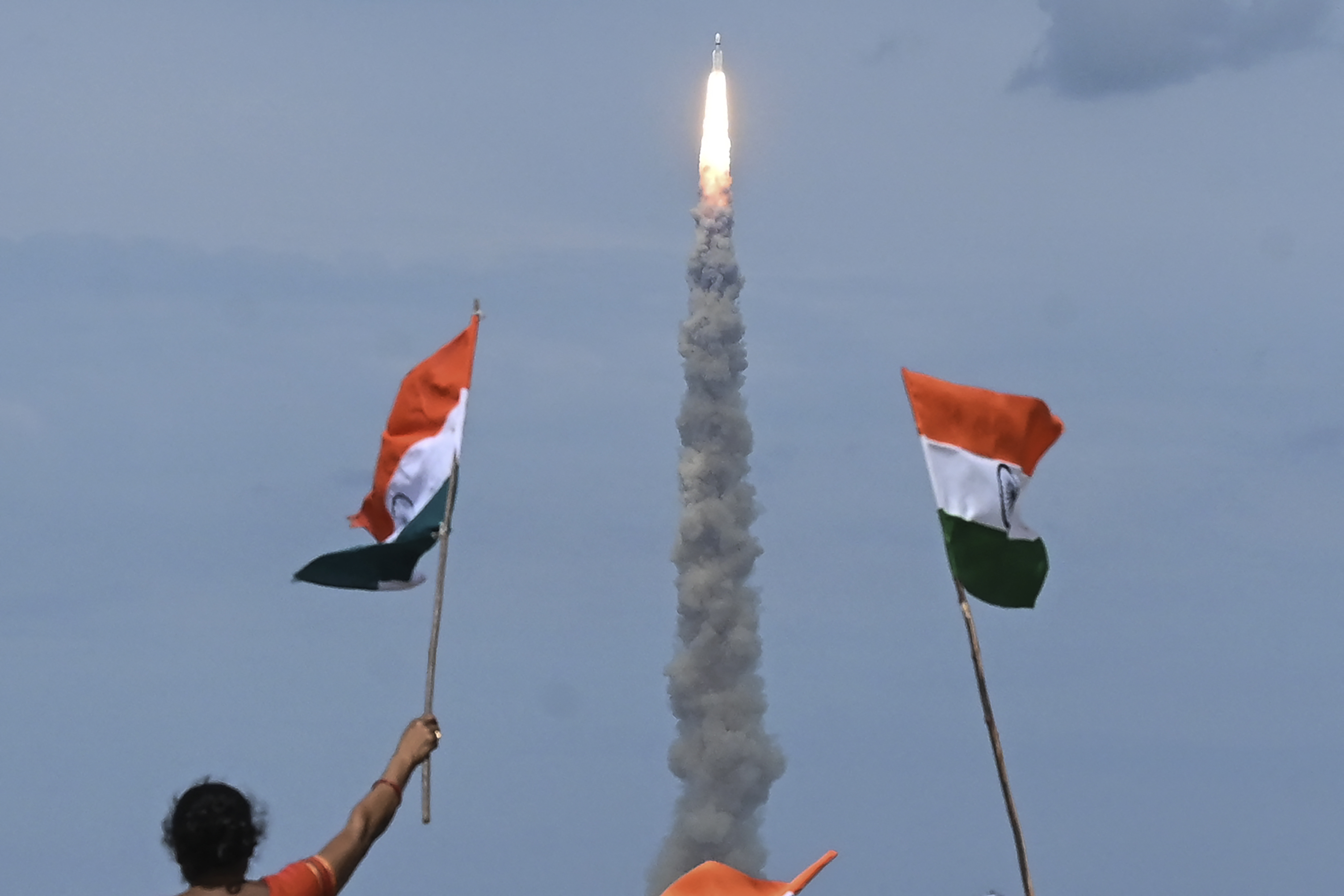People wave Indian flags as an Indian Space Research Organization (ISRO) rocket carrying the Chandrayaan-3 spacecraft lifts off from the Satish Dhawan Space Centre in Sriharikota, an island off the coast of southern Andhra Pradesh state on July 14, 2023. (AFP via Getty Images; AFP or licensors)