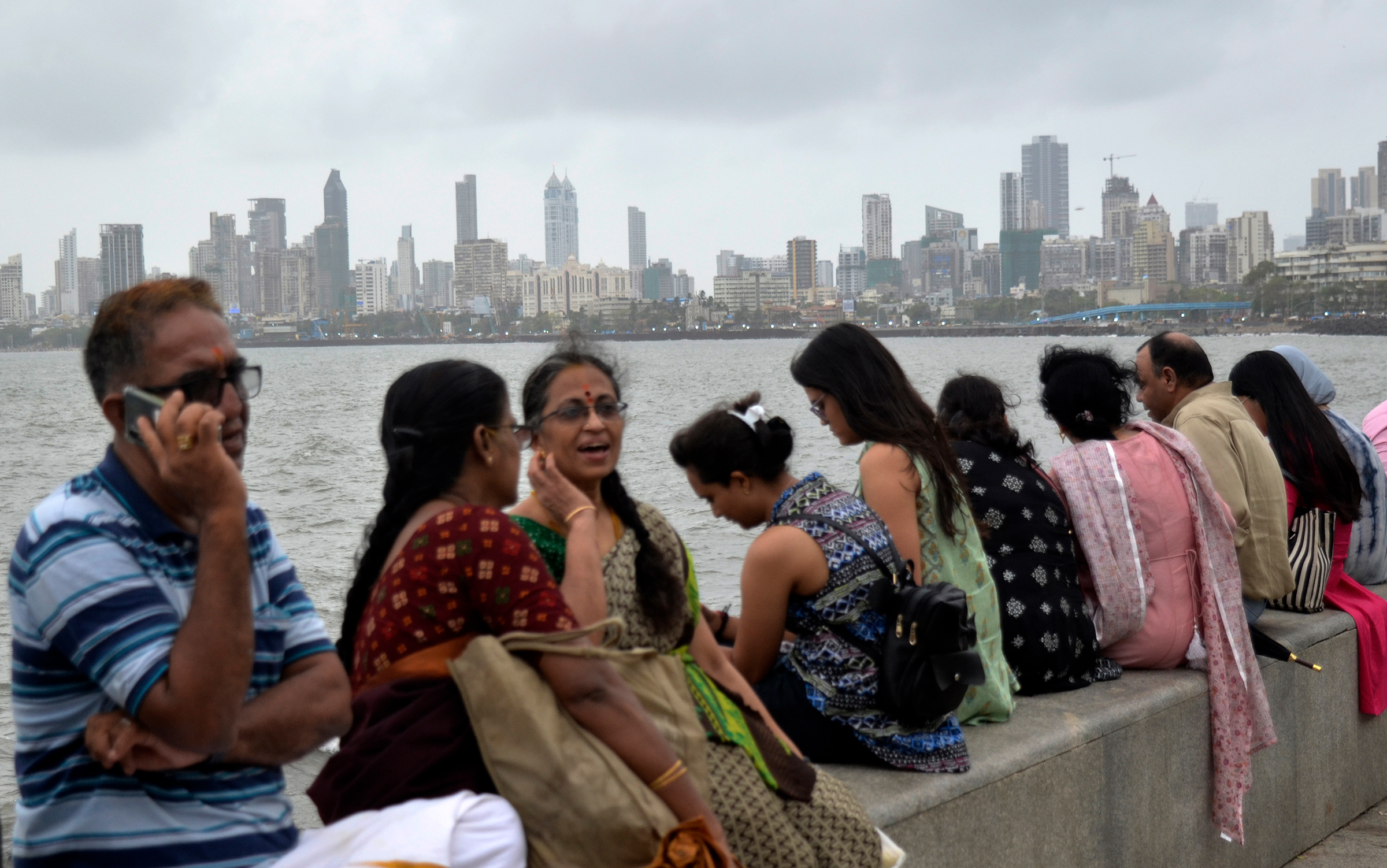 People are seen sitting near marine drive promenade with a cityscape in the background, on the day of World Population Day in Mumbai, India, July 11.